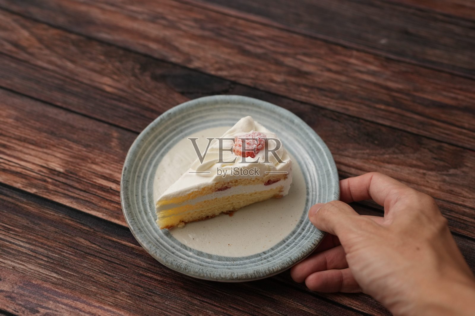 一个黄色人种的手即将吃一块小巧的日本草莓蛋糕,放在一个时尚的日本风格盘子上,背景是棕色的木质甲板。照片摄影图片