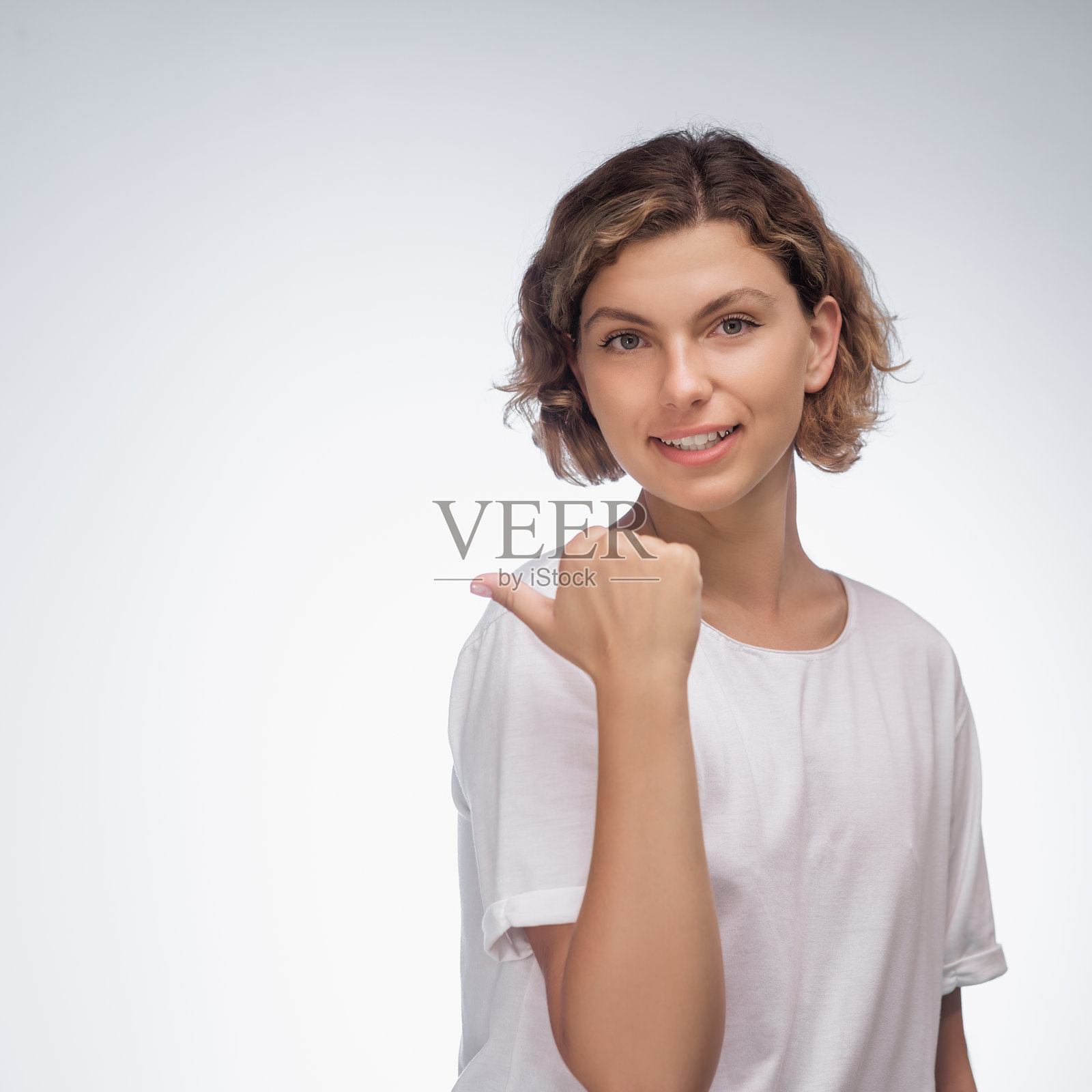 快乐的女性穿着白色T恤,指向蓝色背景后的方向照片摄影图片