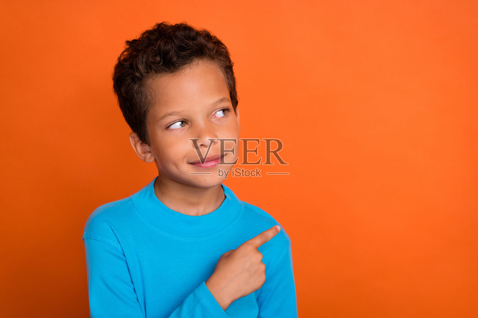 积极友好的男孩用手臂指向空白空间,展示购物促销,背景为橙色。照片摄影图片