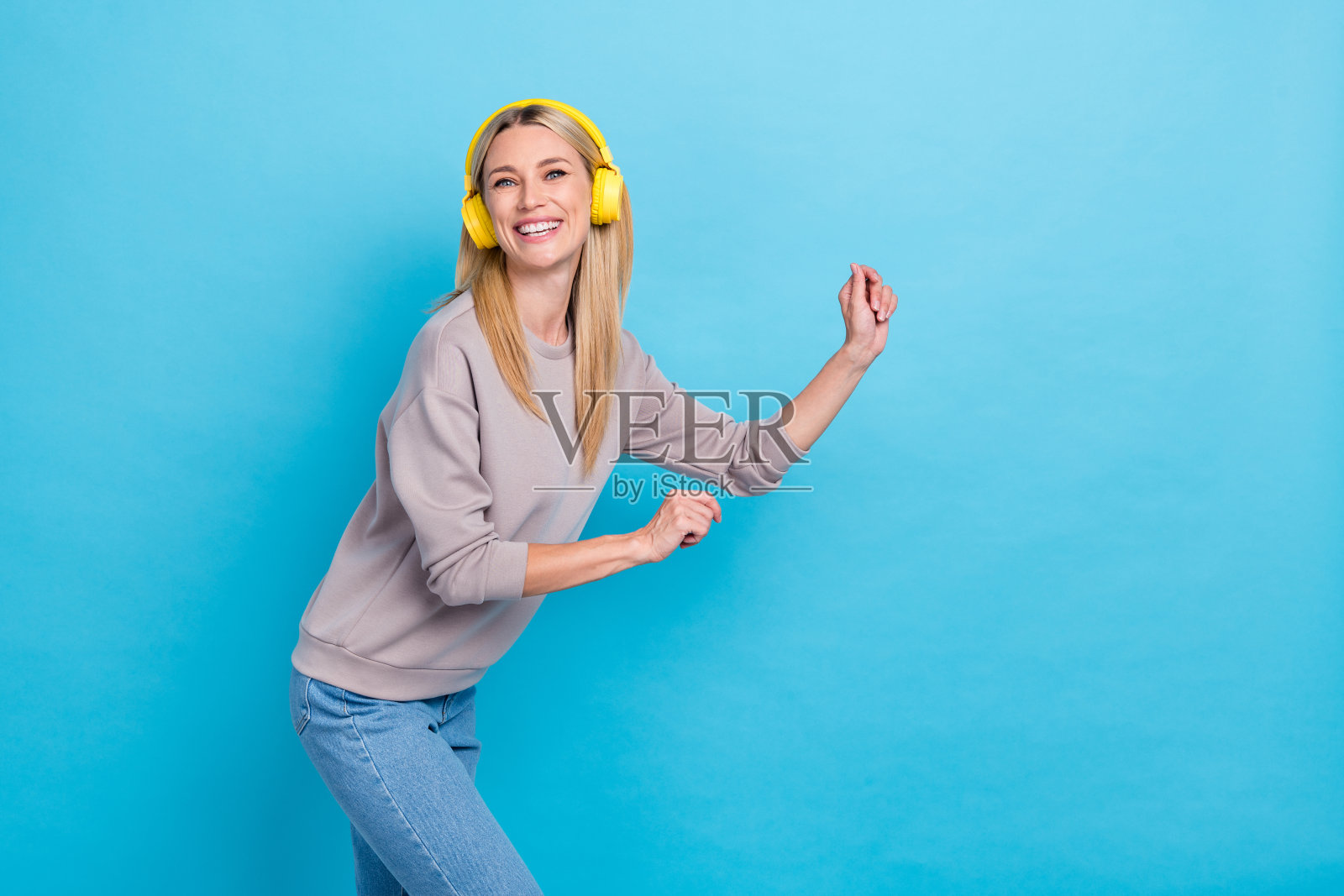 穿着时尚粉彩衣服的积极美丽女士在现代科技商店的空旷空间中欢欣鼓舞,背景为蓝色,价格低廉。照片摄影图片