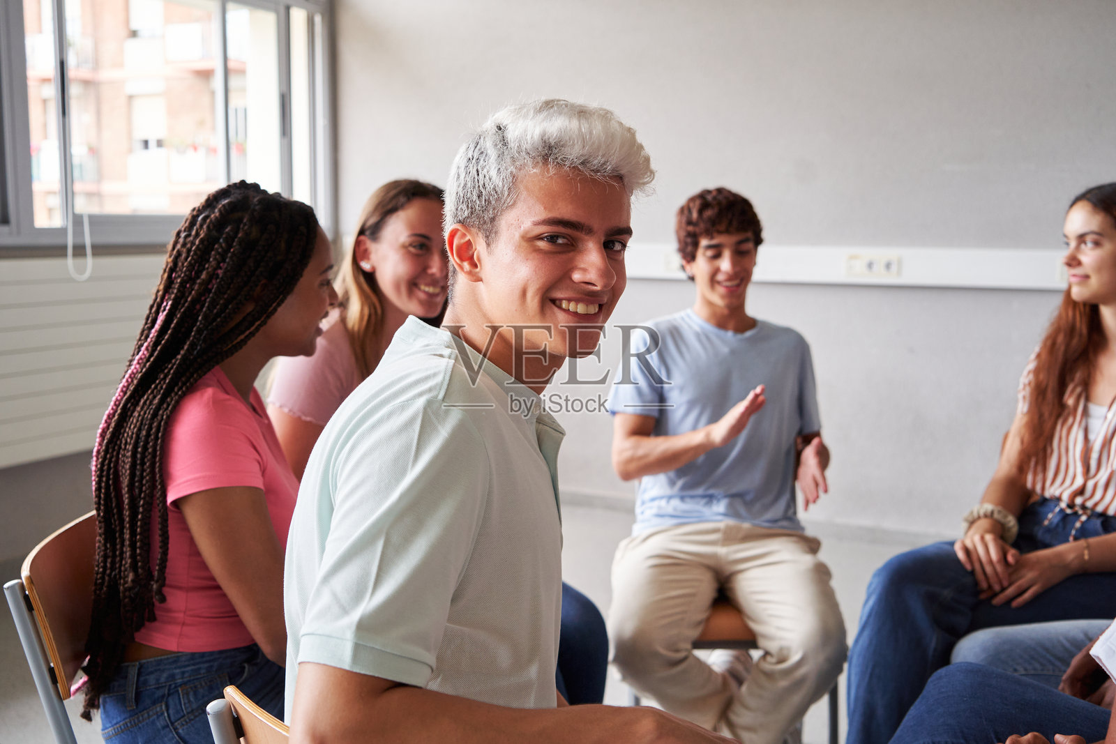 年轻男孩坐在课堂上与同学们围成一圈,面带微笑看向镜头。照片摄影图片