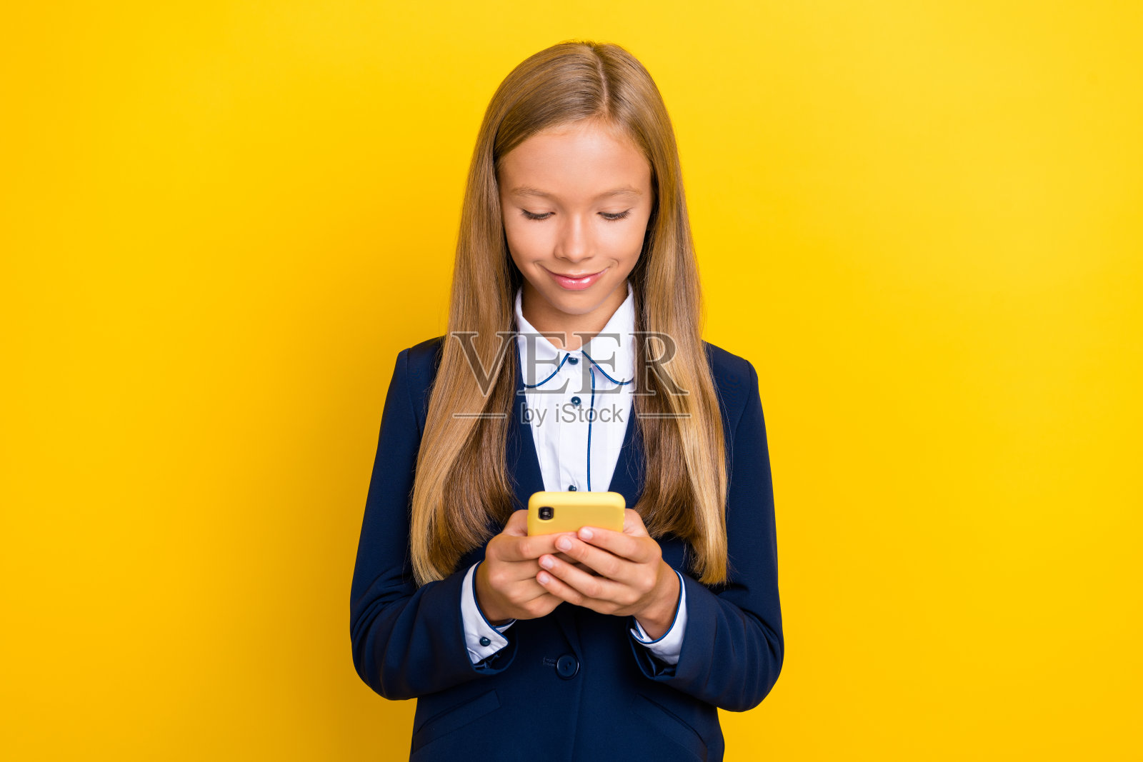 漂亮女孩沉迷于手机,手握设备,正在给同学和朋友发短信,背景为黄色。照片摄影图片