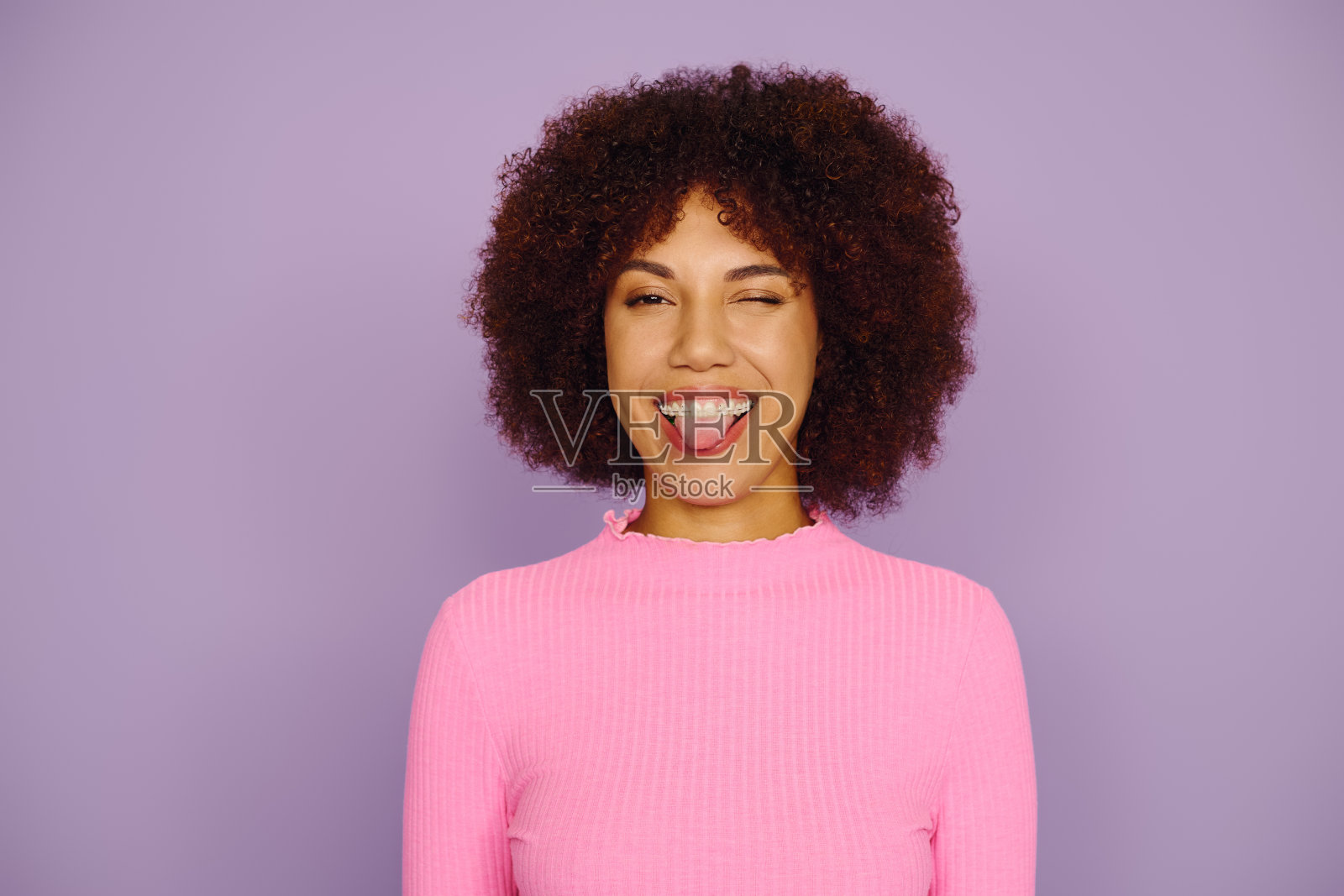 一位快乐的年轻非裔美国女性,卷发俏皮地在明亮的工作室环境中摆姿势照片摄影图片