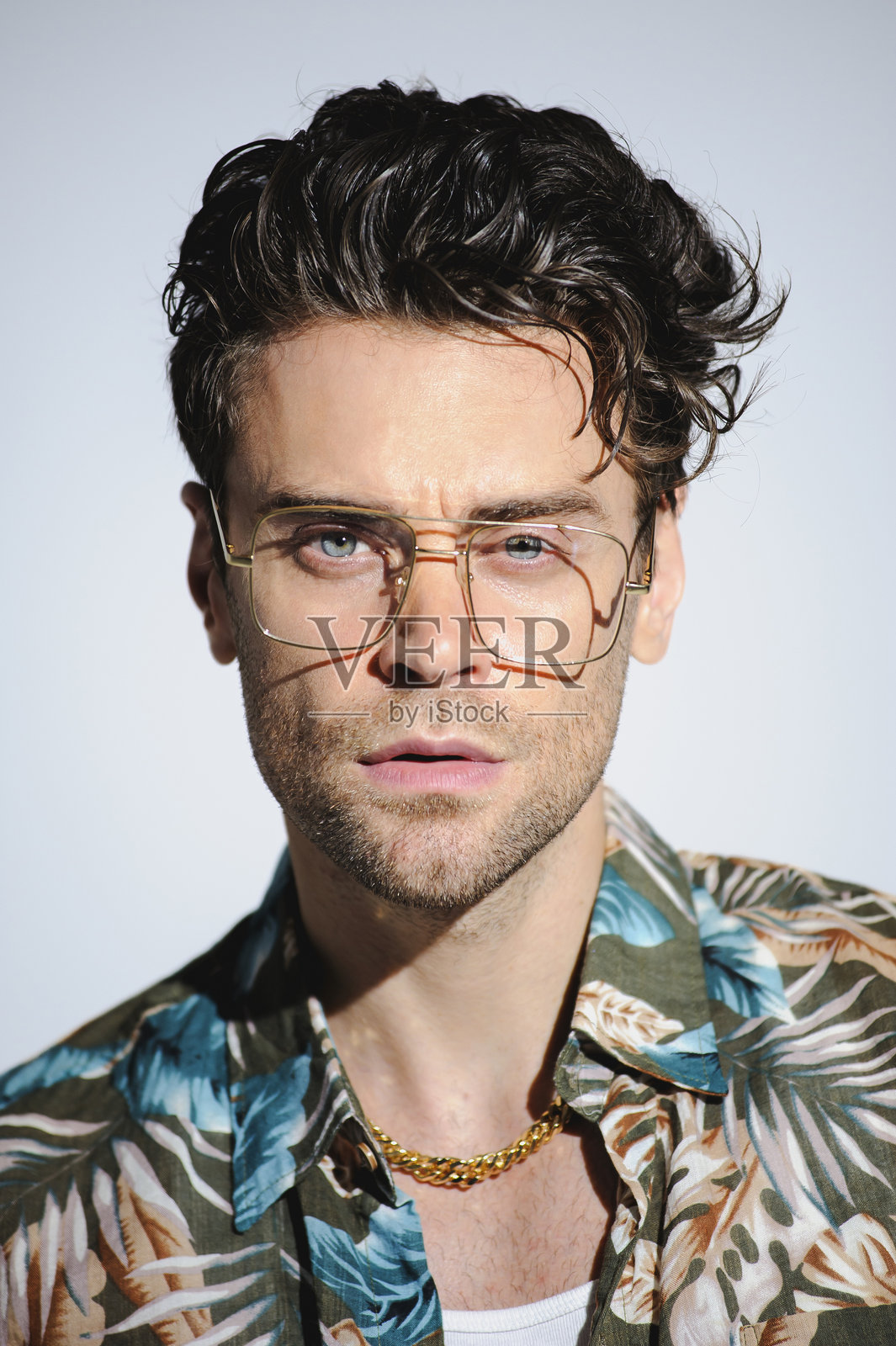 穿着夏威夷印花衬衫和奢华眼镜的时尚男士肖像,正对着镜头,背景为灰色。照片摄影图片