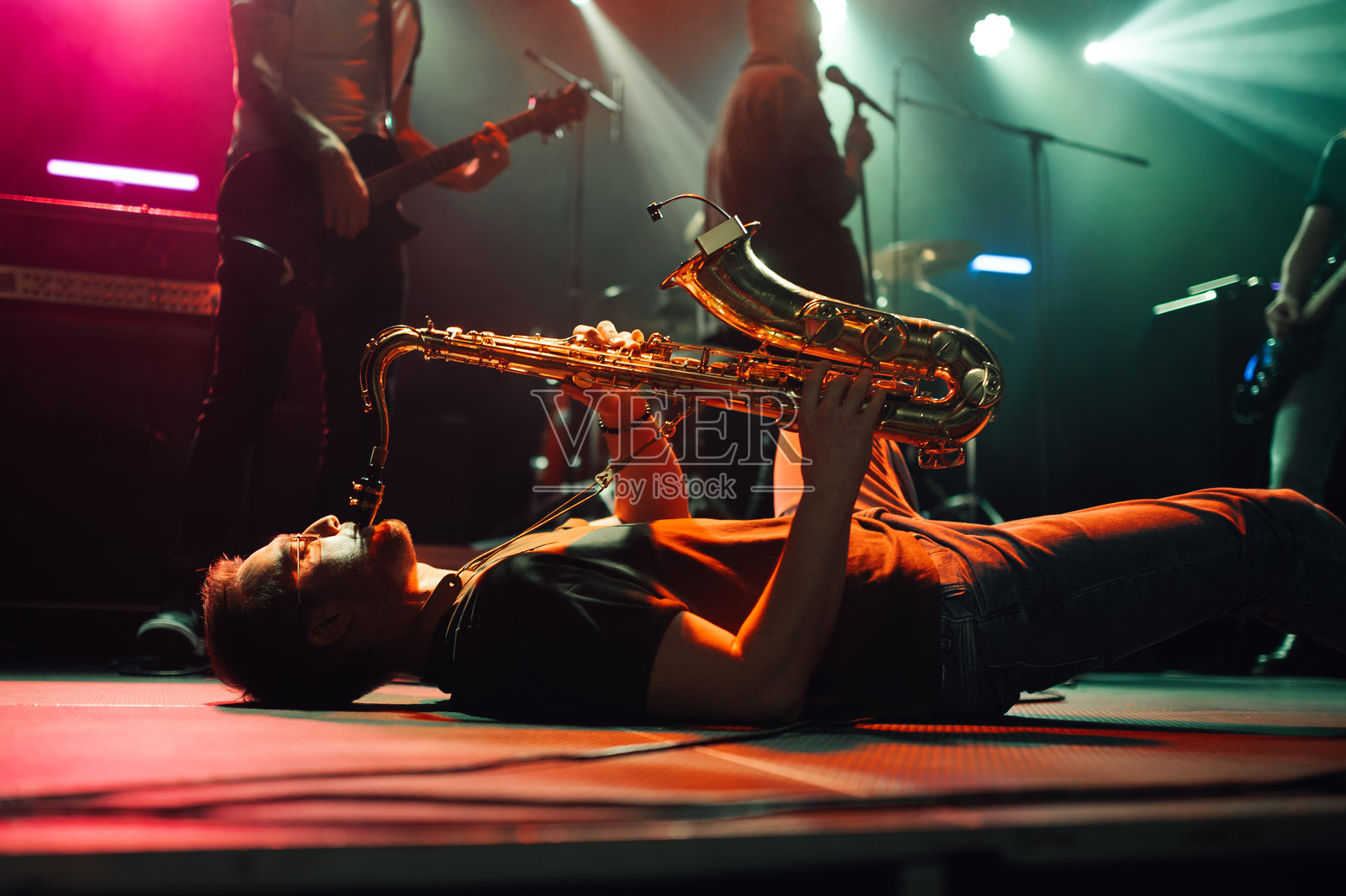 在音乐会上,萨克斯演奏者躺着演奏萨克斯风。照片摄影图片