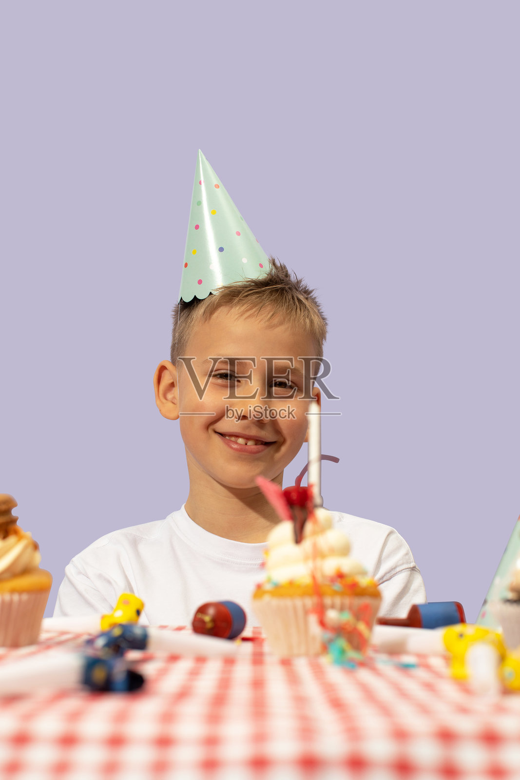 微笑的男孩戴着生日帽,手里拿着装饰精美的杯子蛋糕照片摄影图片