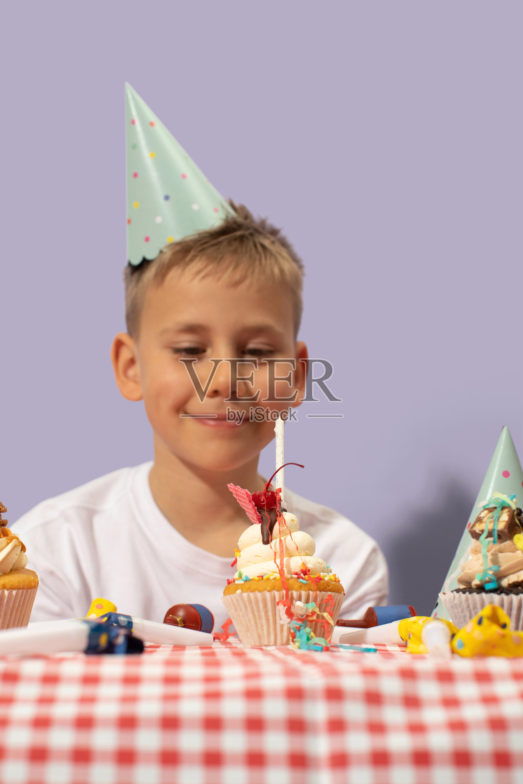 微笑的男孩戴着生日帽,手里拿着装饰精美的杯子蛋糕照片摄影图片
