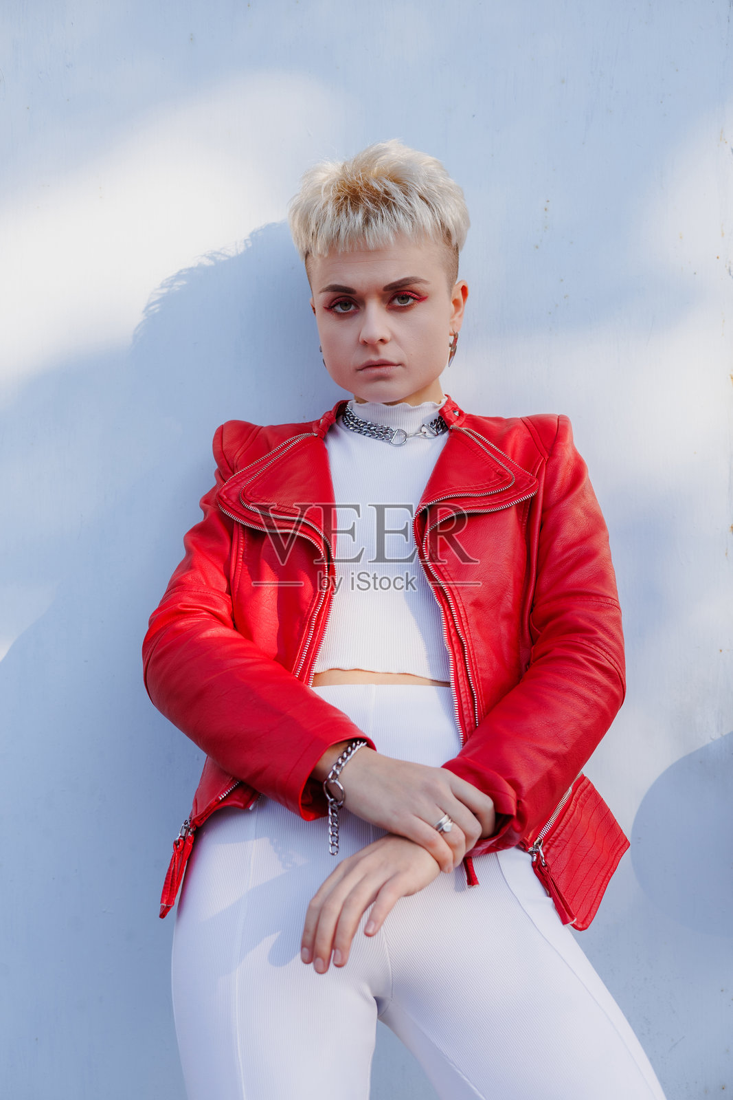 穿着红色皮夹克的时尚短发女性在灰色背景下注视镜头,身后有阴影。照片摄影图片