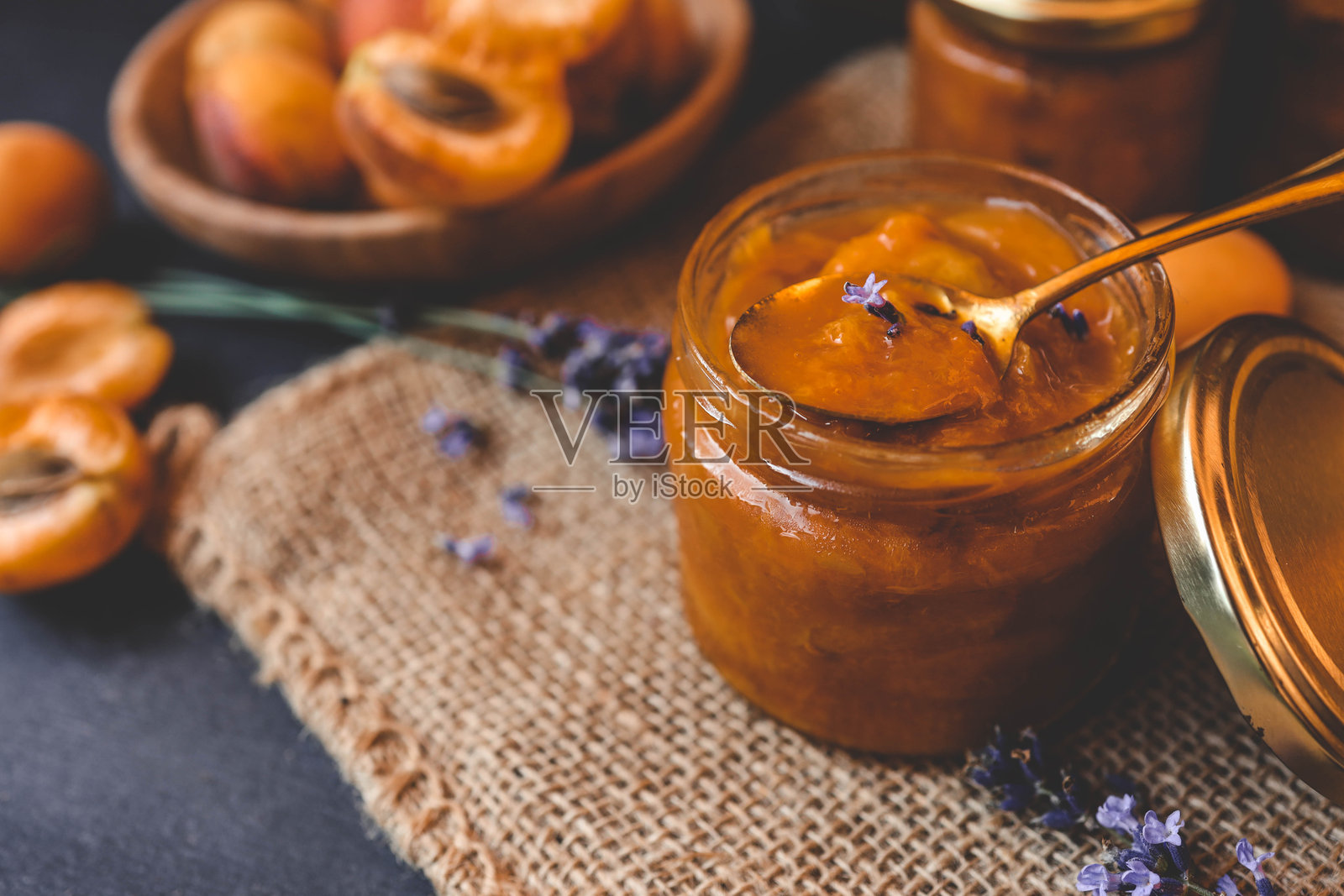 自制的杏子果酱配以薰衣草花,周围是新鲜的杏子和薰衣草枝,摆放在质朴的麻布上。照片摄影图片