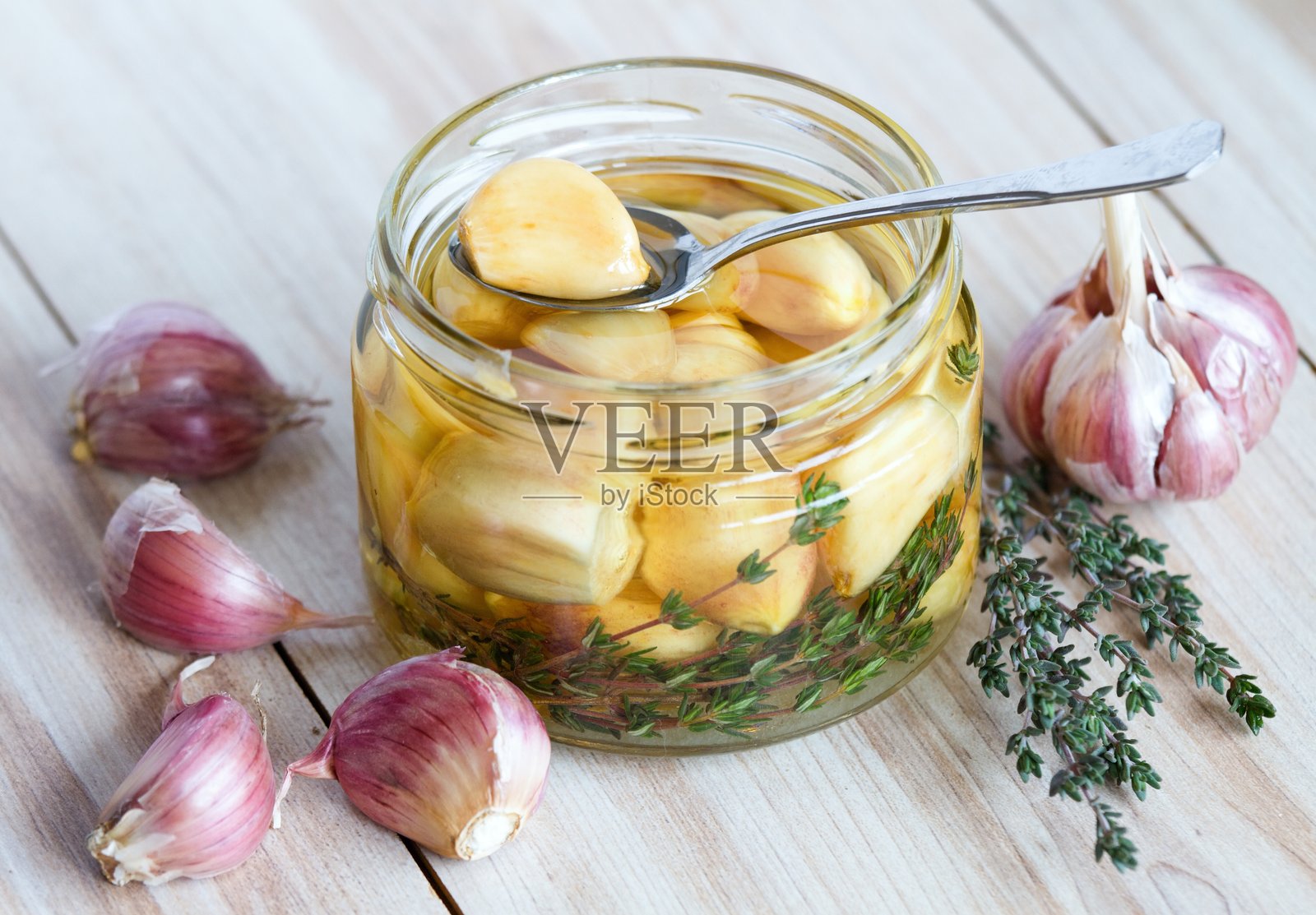 盛有大蒜瓣、葵花籽油和百里香腌制的勺子。照片摄影图片