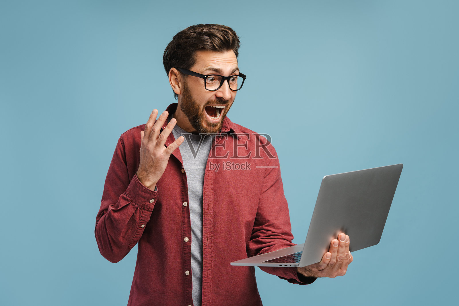 戴眼镜的快乐惊讶的胡子男人,手持笔记本电脑,观看视频的肖像照片摄影图片