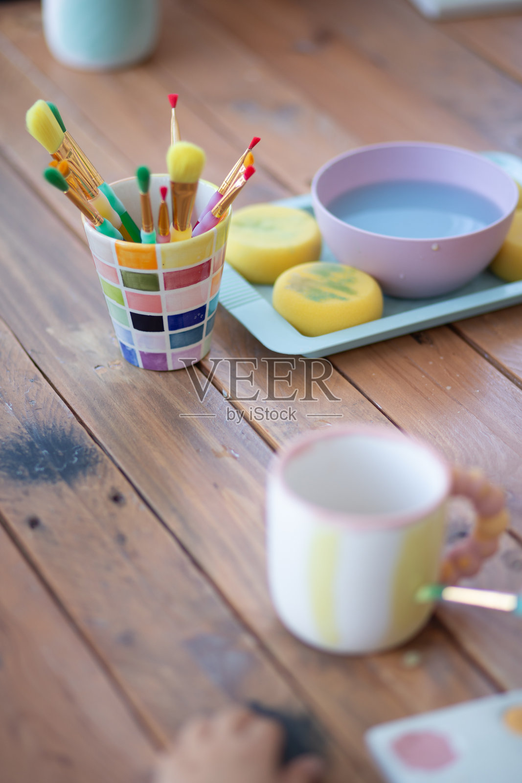 许多画笔放在一个罐子里,正在木桌上为一个杯子作画照片摄影图片