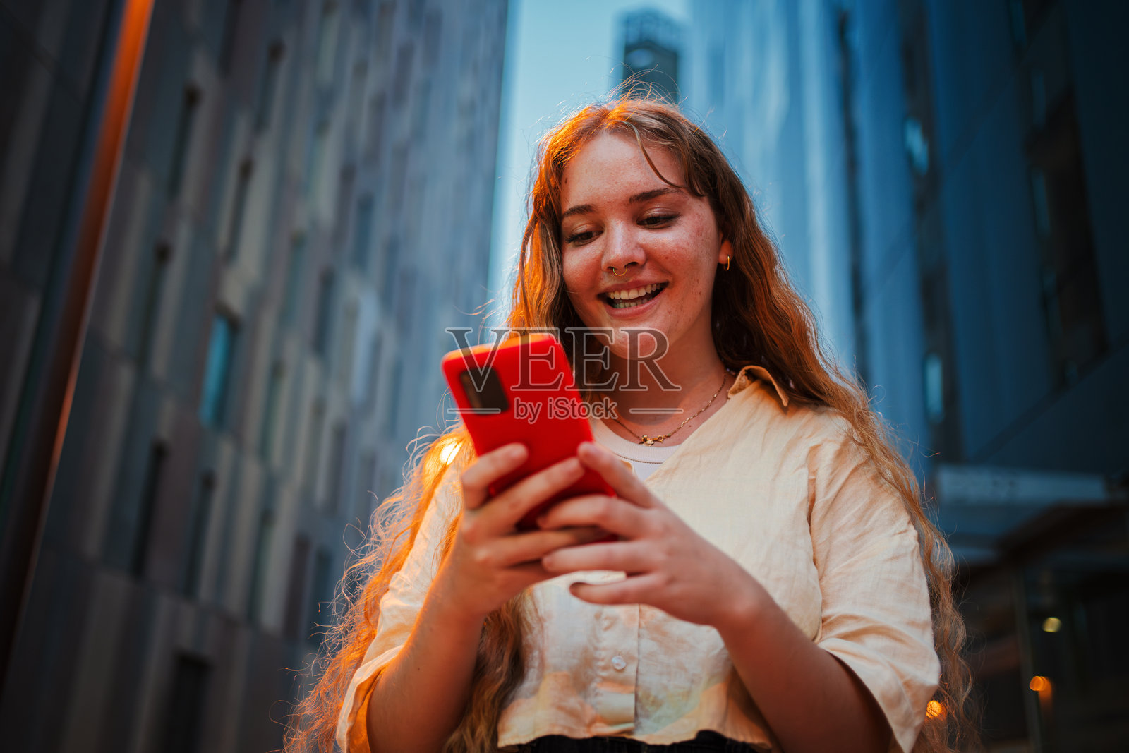 微笑的年轻女性在城市夜晚使用智能手机,街灯照亮了周围。非常适合科技、沟通、社交媒体或夜晚城市生活的概念。照片摄影图片