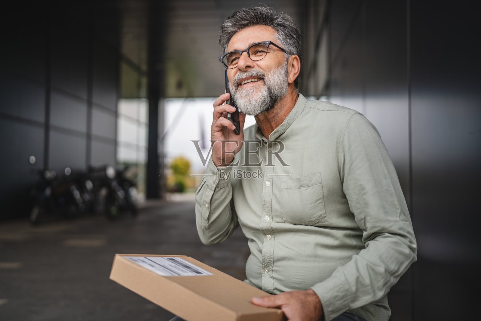 男子坐在长椅上,面前放着包裹,正在用手机通话。照片摄影图片