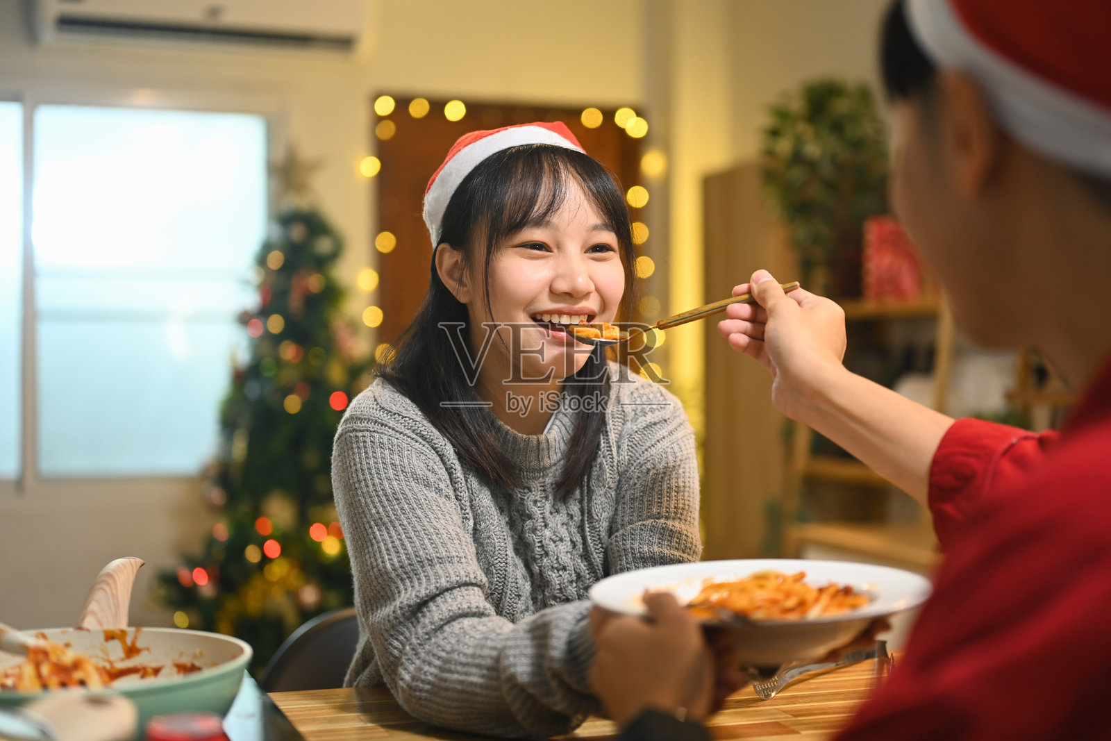 快乐的年轻情侣戴着圣诞帽在温馨装饰的厨房里共享美好的一餐照片摄影图片