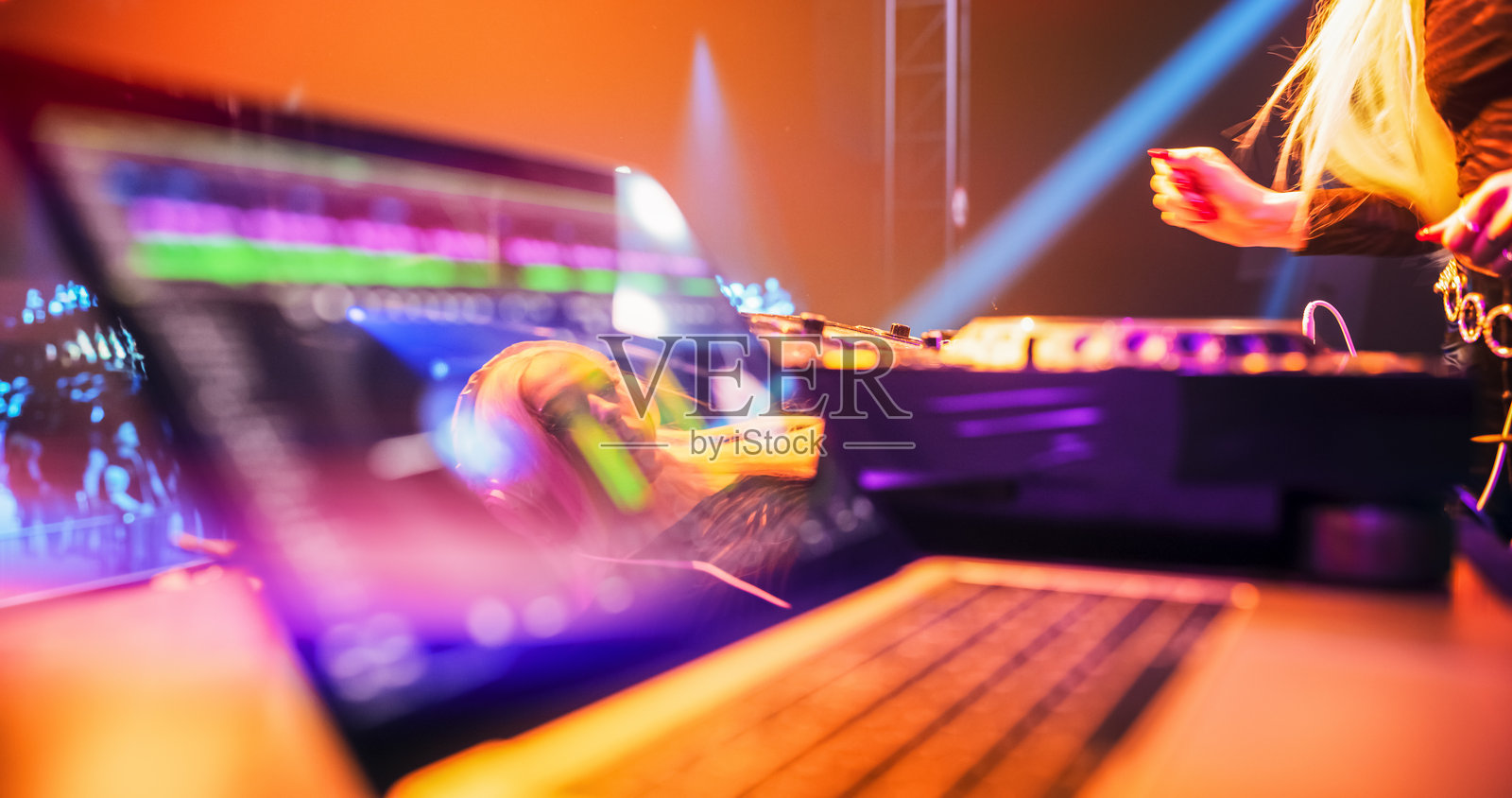 舞台上桌子上的笔记本电脑,运行着DJ音乐软件。美丽的女性音乐制作人在表演时,凝视着显示屏。照片摄影图片