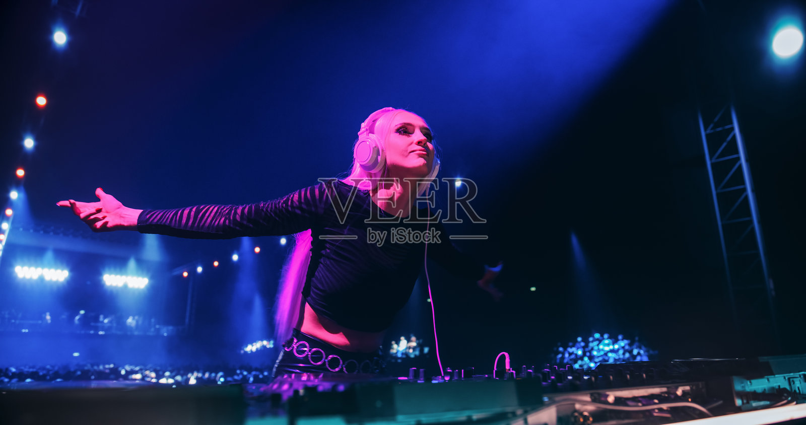 身穿黑色服装的女性流行音乐人在俱乐部舞台上演奏电子和浩室音乐,激情四溢地在调音台后跳舞,明亮而生动的灯光下营造出充满活力的音乐会氛围。照片摄影图片