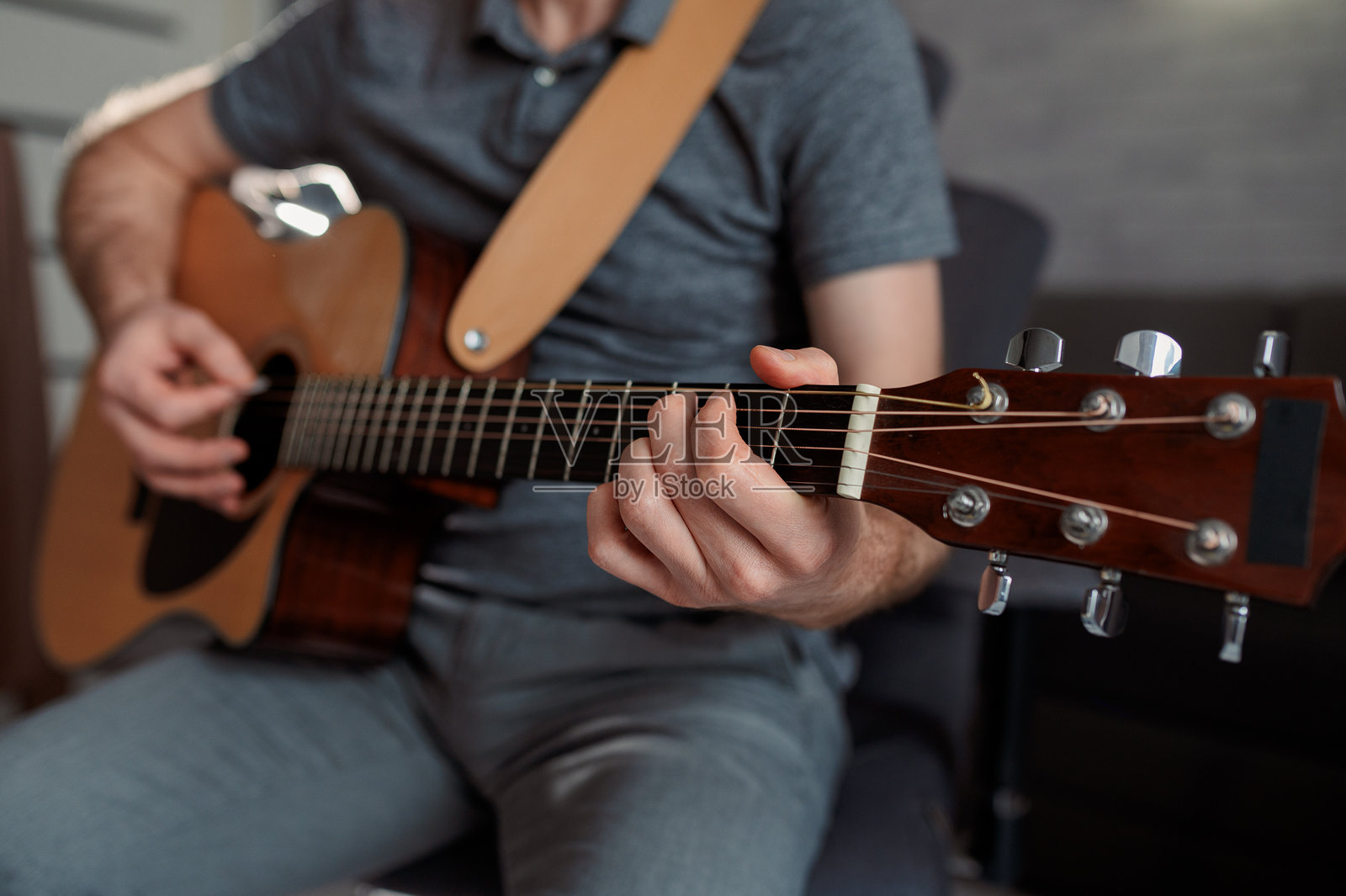 男音乐家坐在沙发上,在办公室里弹奏原声吉他。照片摄影图片