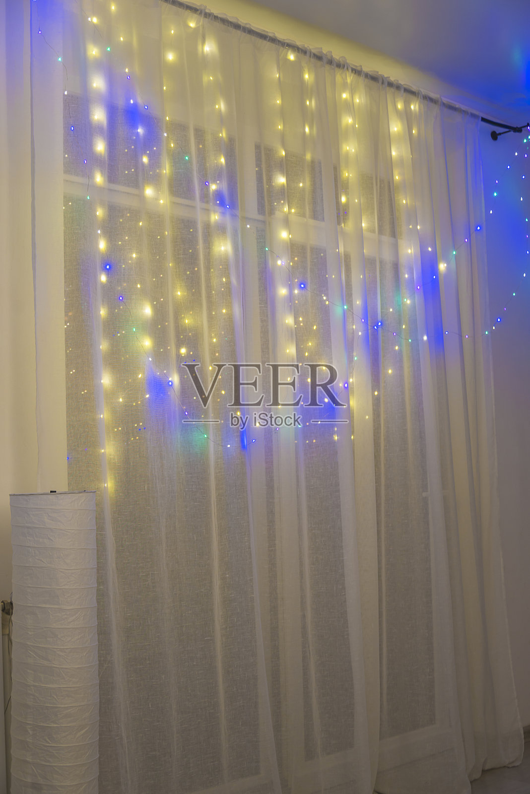 窗户上的白色窗帘与房间内的圣诞灯饰花环照片摄影图片