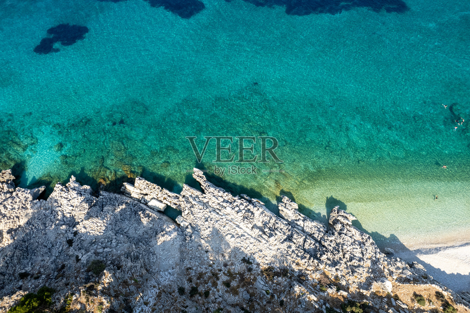 阳光明媚的夏日,绿松石色的海水与岩石海岸相遇照片摄影图片