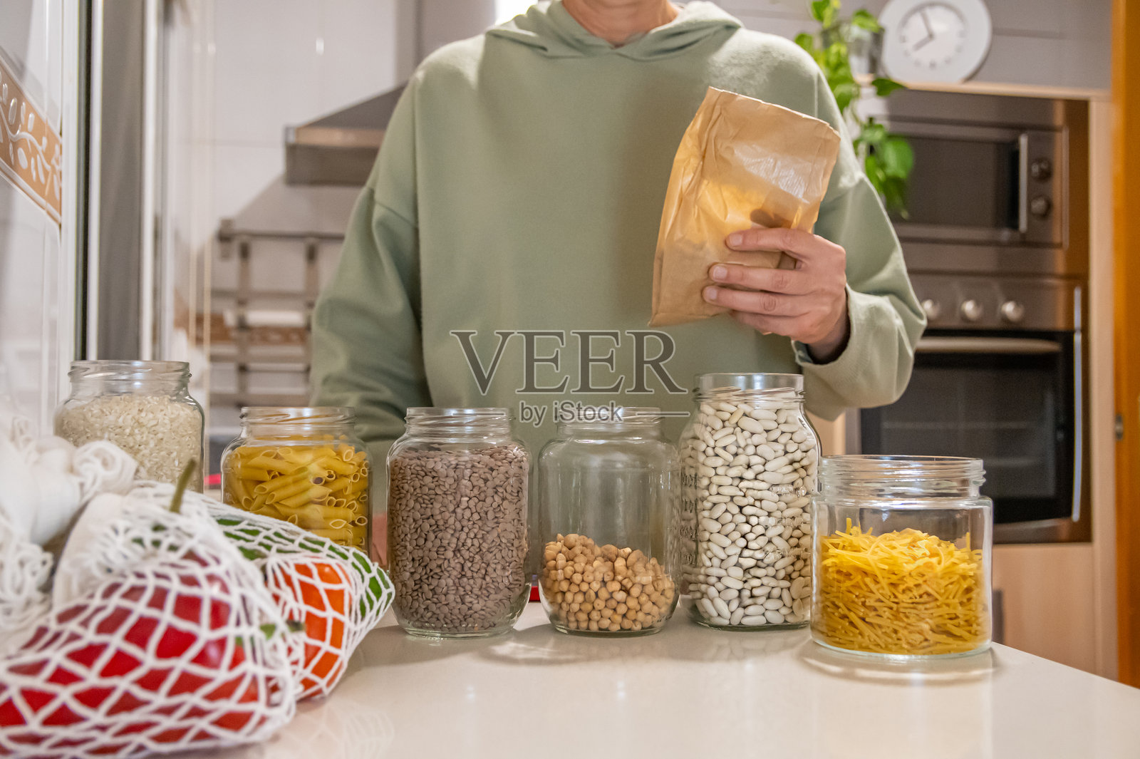 一个人正在进行大宗商品购买,并将其包装在玻璃罐中。这个未被识别的个体注重环保,使用纸袋和网袋进行日常购物。照片摄影图片