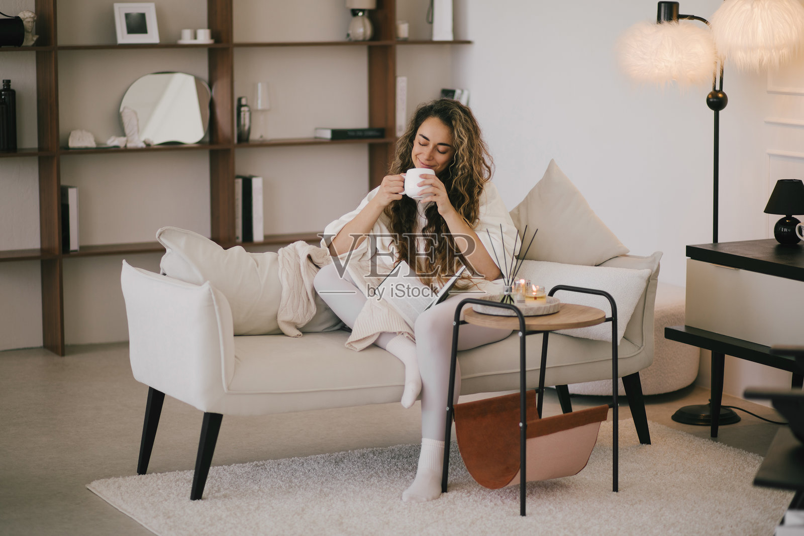 年轻女性坐在舒适的客厅沙发上,阅读书籍并喝茶。照片摄影图片