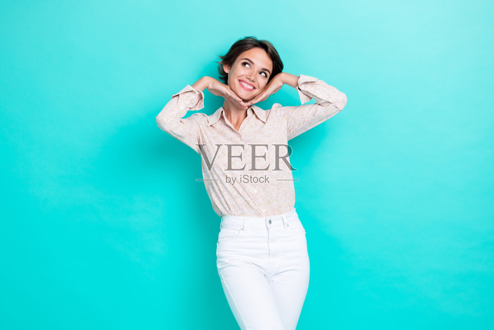 甜美漂亮时尚的女士用手触摸脸庞,眼神充满兴趣,仿佛在空旷的空间中梦想和想象约会,背景为青色。照片摄影图片