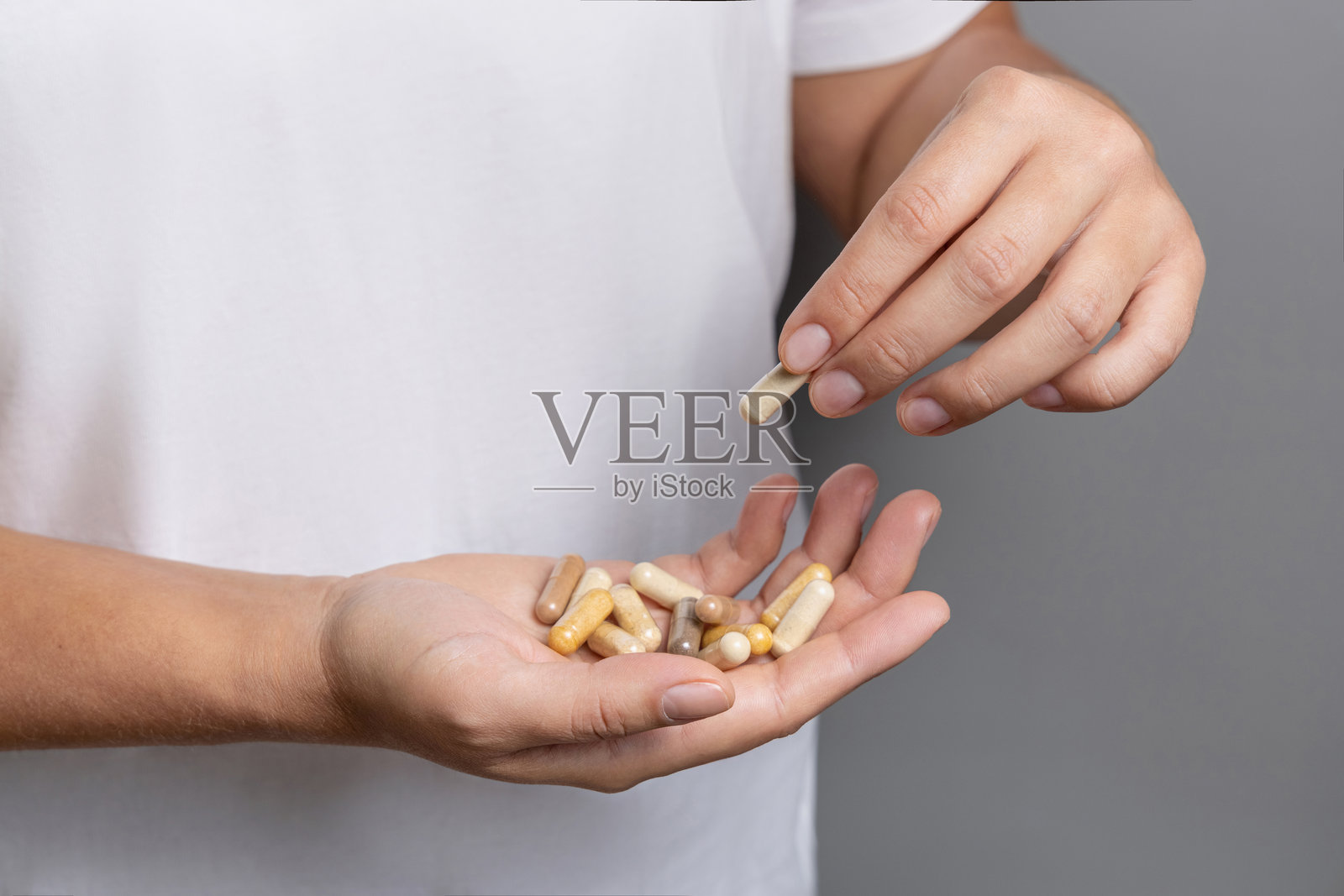 女人手中拿着米色的草药胶囊,近距离拍摄,背景为白色衬衫。照片摄影图片