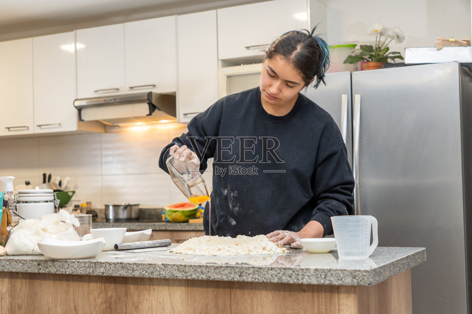 年轻的拉丁裔女性,黑发扎起,正在将生鸡蛋放入面粉中制作面团照片摄影图片