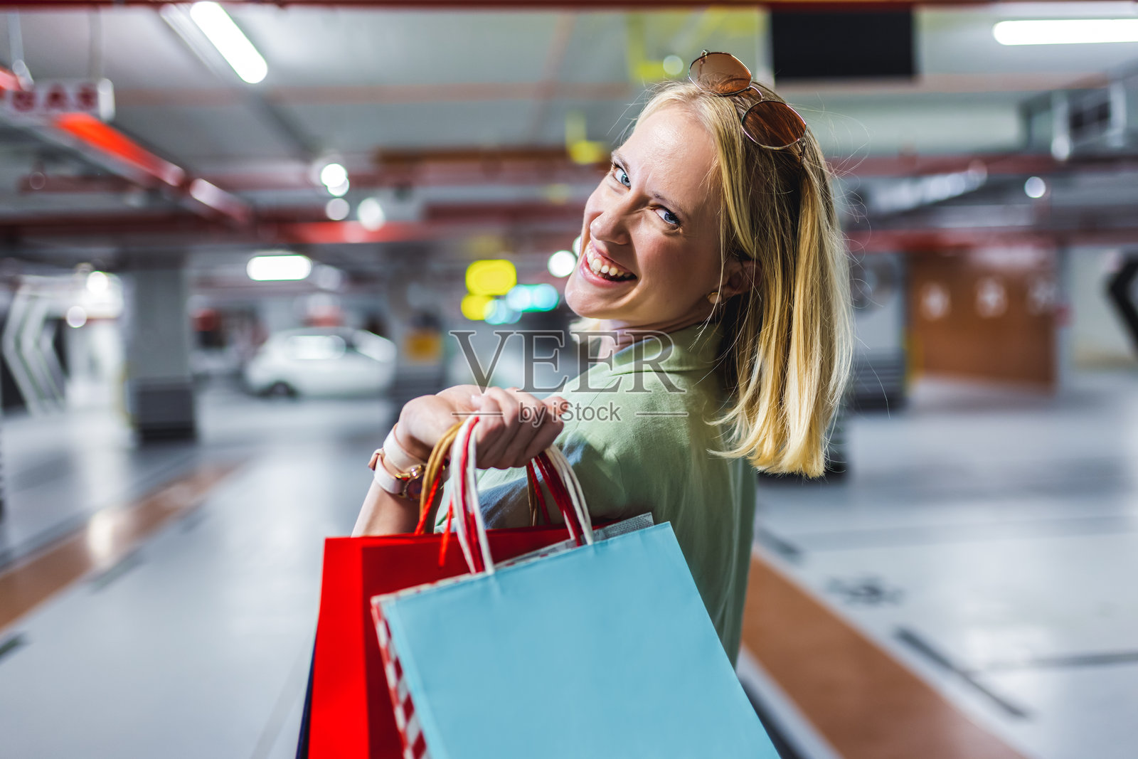 金发女性提着购物袋在地下车库里走动的肖像。照片摄影图片