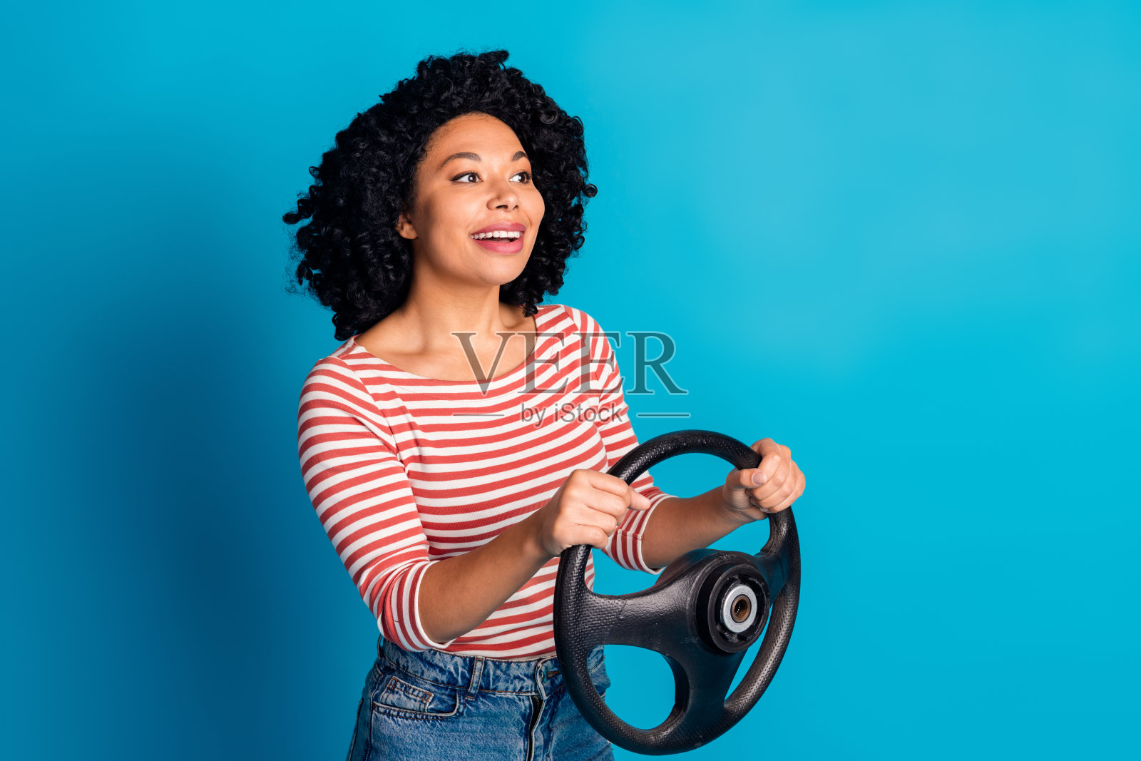 可爱的女孩穿着时尚的衣服,手握方向盘,背景为蓝色,空旷的空间。照片摄影图片