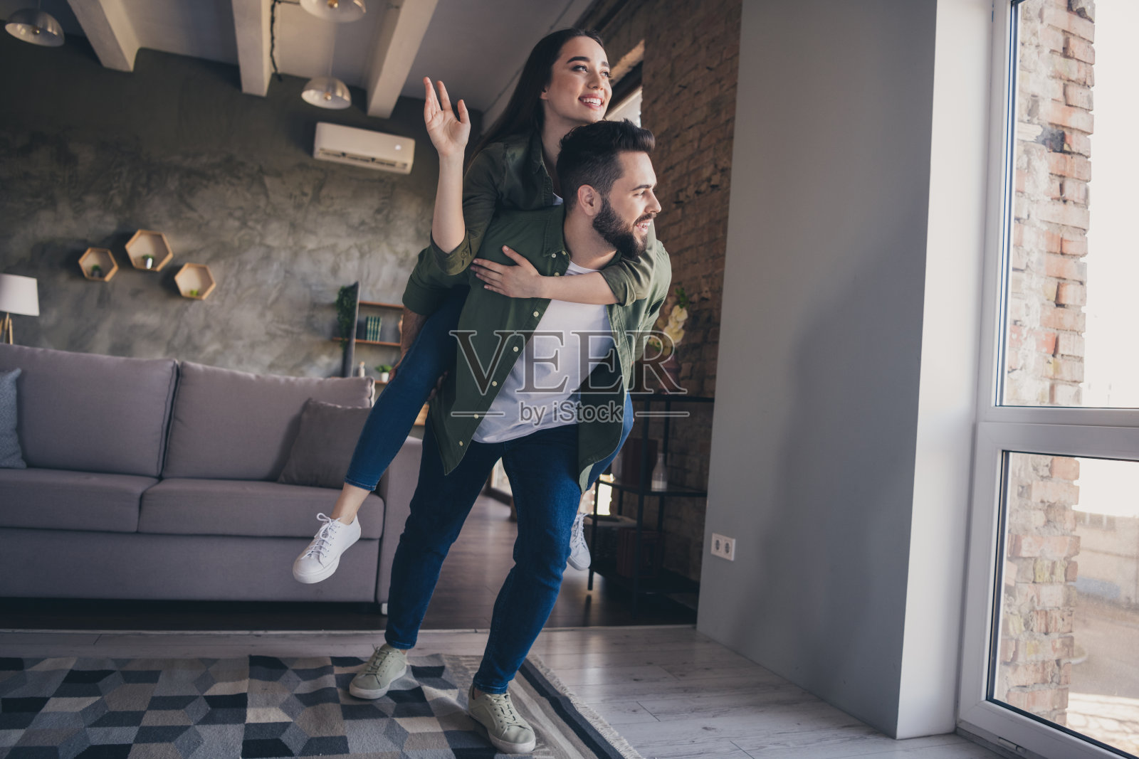 一对迷人快乐的已婚夫妇穿着休闲衬衫,在室内房间里开心地挥手打招呼。照片摄影图片