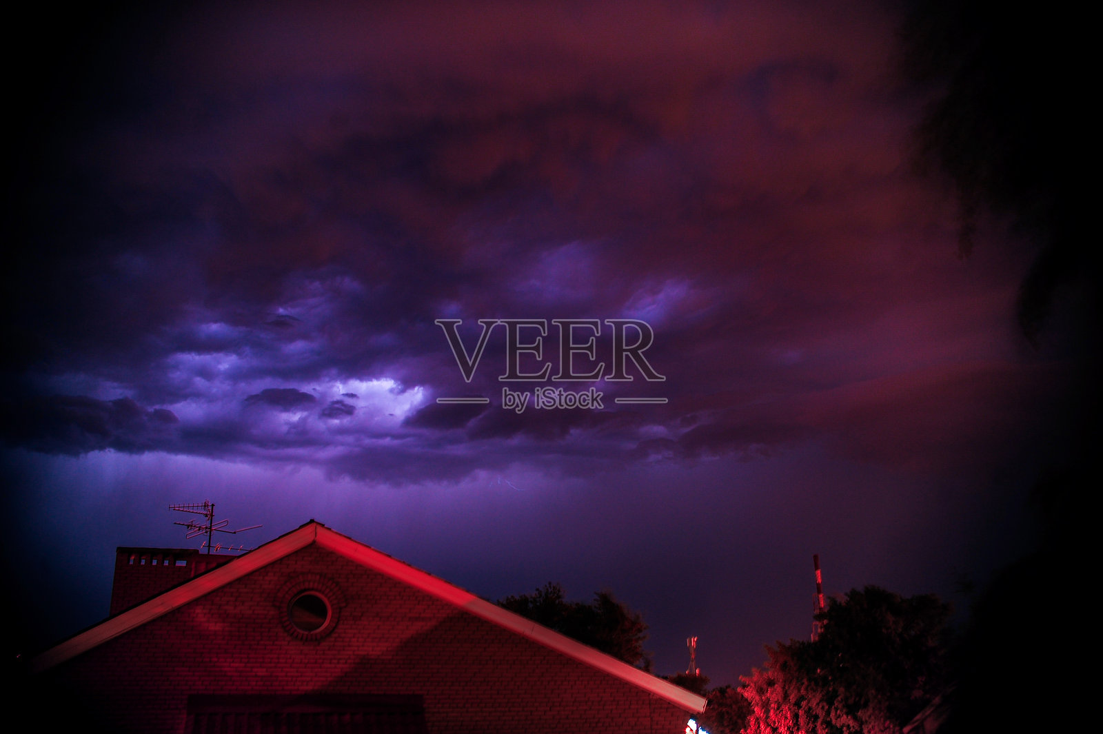 一座鲜艳的红色房子在戏剧性的紫色天空下格外显眼,照片摄影图片