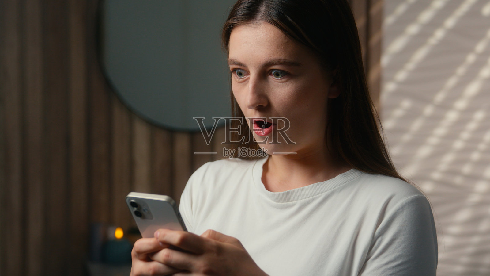 惊讶快乐的白人女性在家浴室里阅读手机信息,感到震惊、惊讶和欣喜,取得了在线成功,成为女性赢家,手机成瘾的女士获得了折扣。照片摄影图片