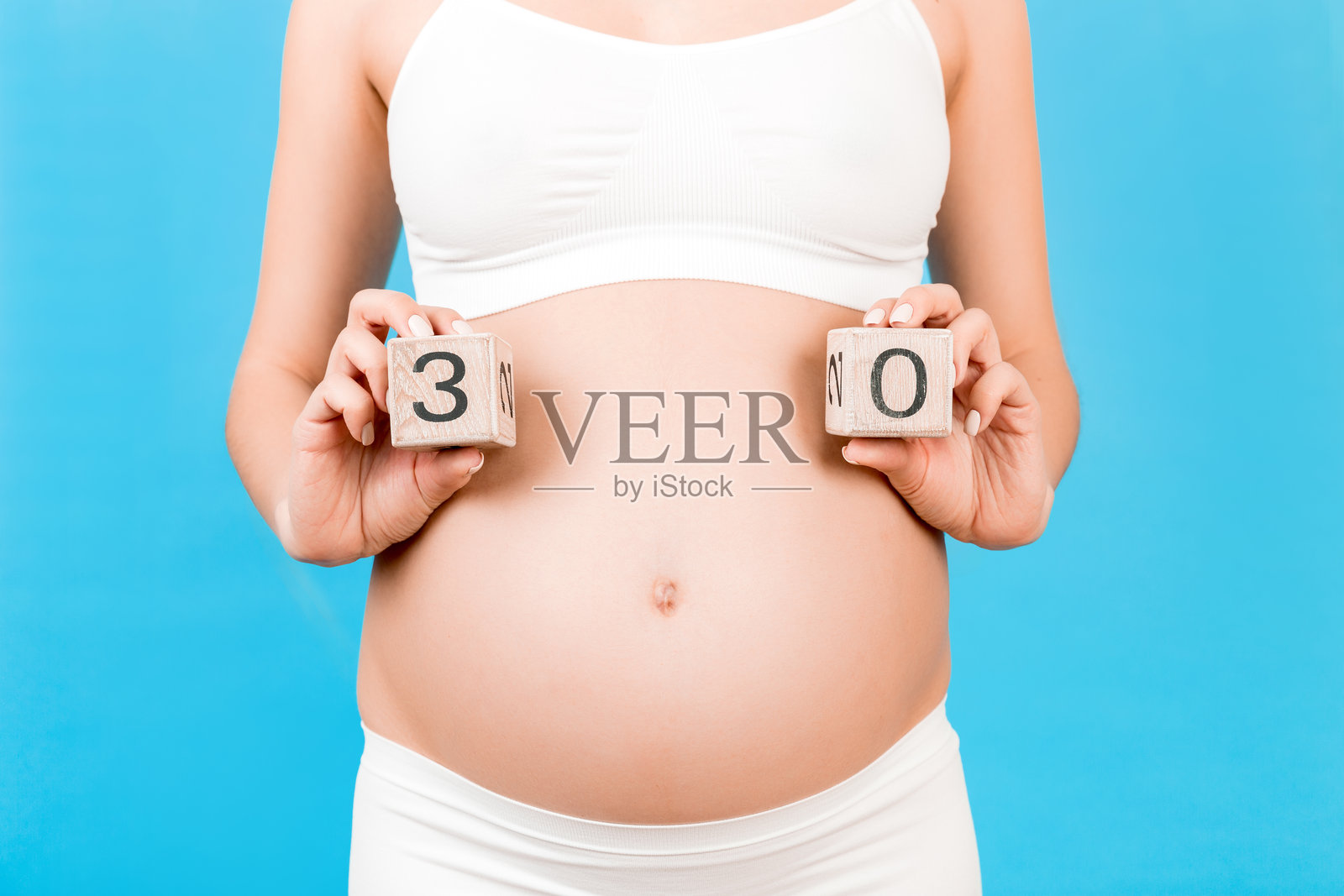 孕妇穿着白色内衣,近距离肖像,肚子上放着显示怀孕三十周的方块,背景为蓝色。期待宝宝。留白空间。照片摄影图片