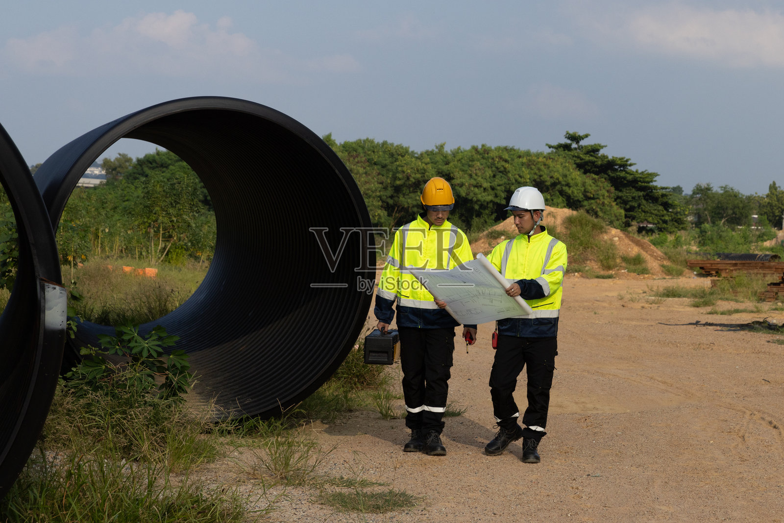 两名男性项目工程师一起走到指定的区域,勘测在社区和住宅区附近新建道路时钻孔排水管的地点。照片摄影图片