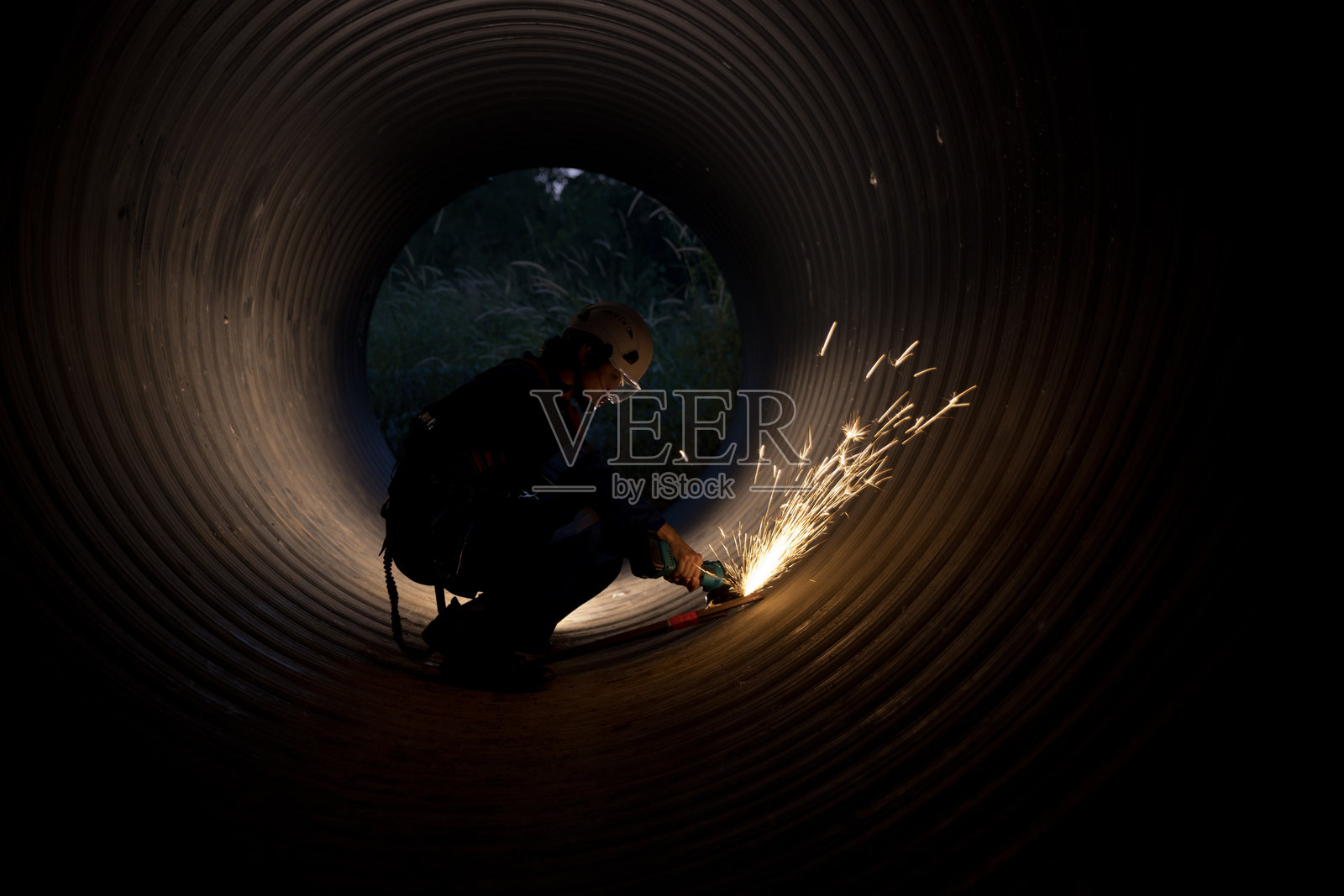 一名建筑工人在排水管内自信地进行工作,熟练地打磨以制作项目的重要部分。火花四溅,他展示了自己的专业技能,这对推动施工进展至关重要。照片摄影图片