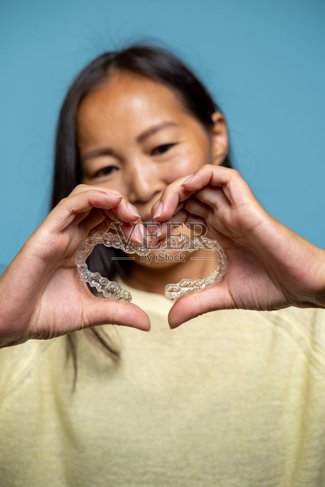 一位女性手持透明牙齿矫正器,呈心形。照片摄影图片