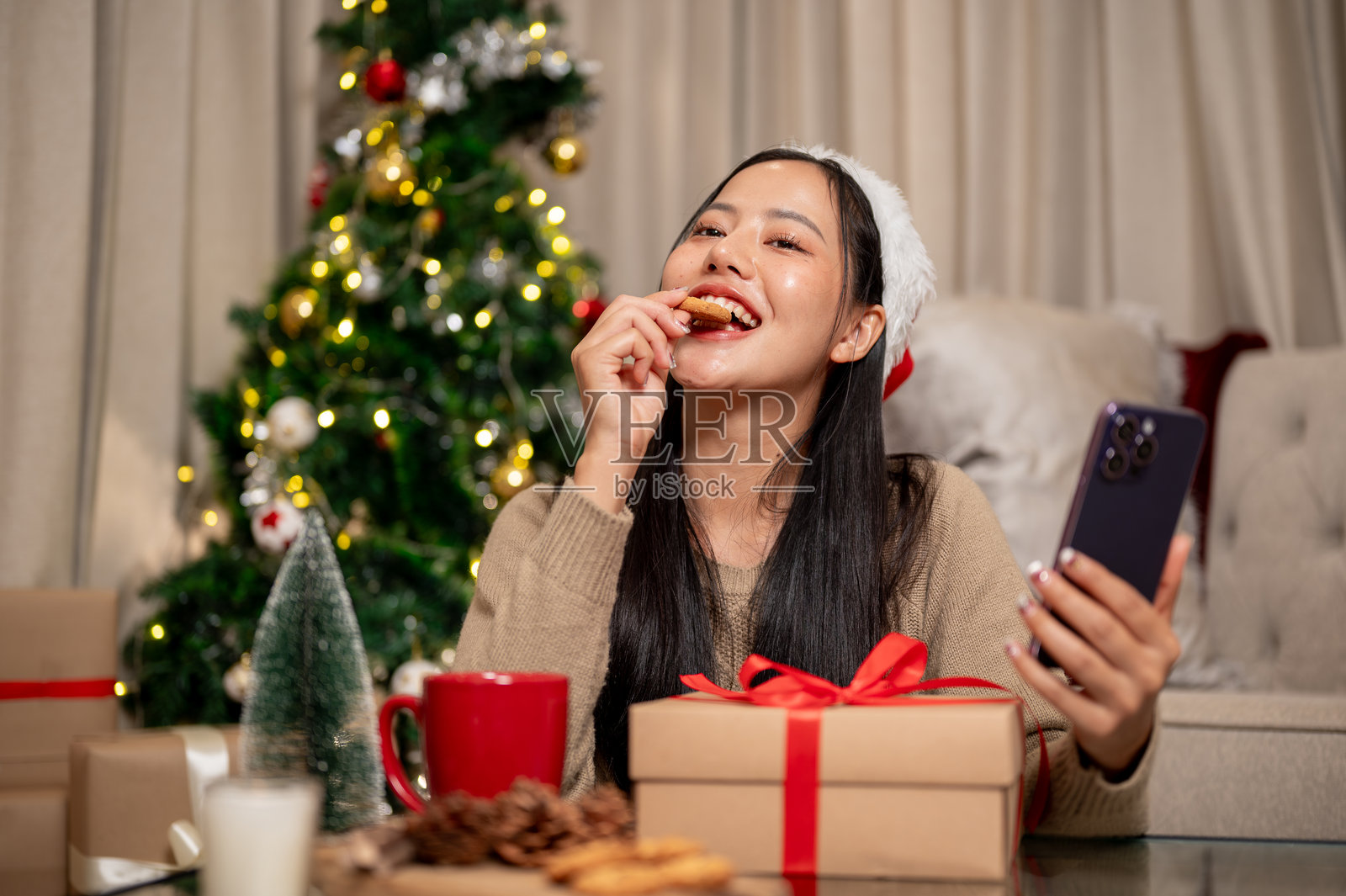 一位迷人、快乐的亚洲女性在咖啡桌上享受圣诞饼干。照片摄影图片