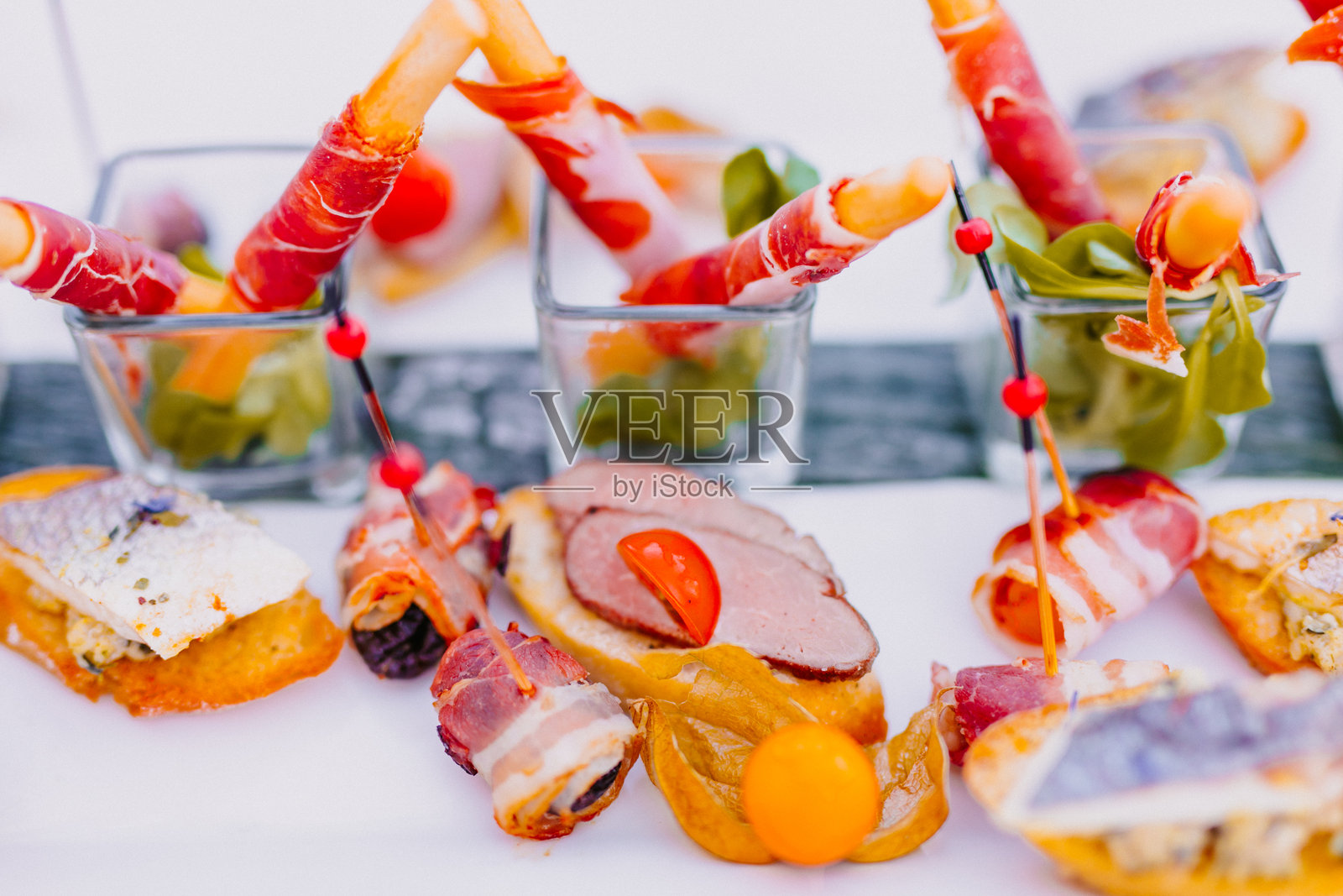 脆脆的饼干棒裹着西班牙熏火腿,精美地陈列在小玻璃杯中的芝麻菜叶上。照片摄影图片