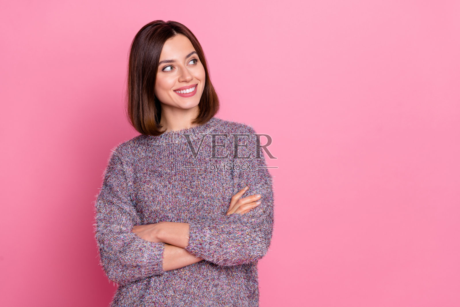 迷人的棕发女孩微笑着,双臂交叉,思考着,背景为粉色渐变色,留有空白空间。照片摄影图片
