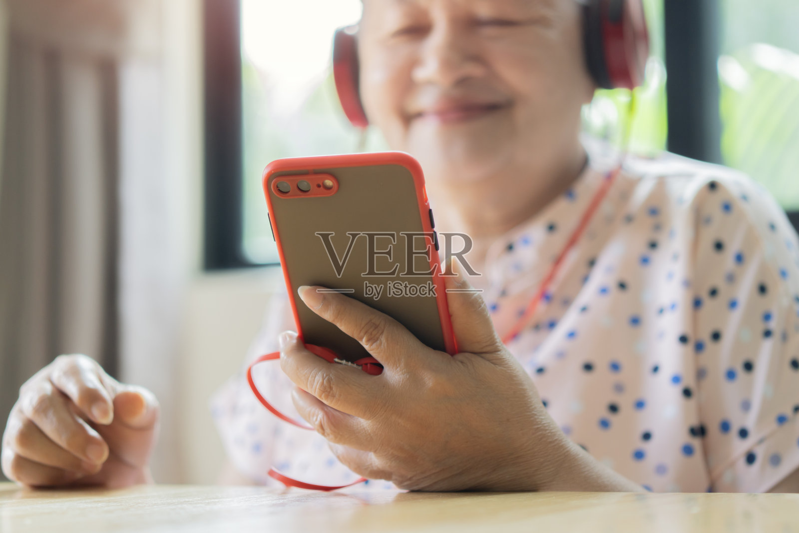 现代亚洲老年女性戴着耳机,笑着用智能手机观看网络视频照片摄影图片