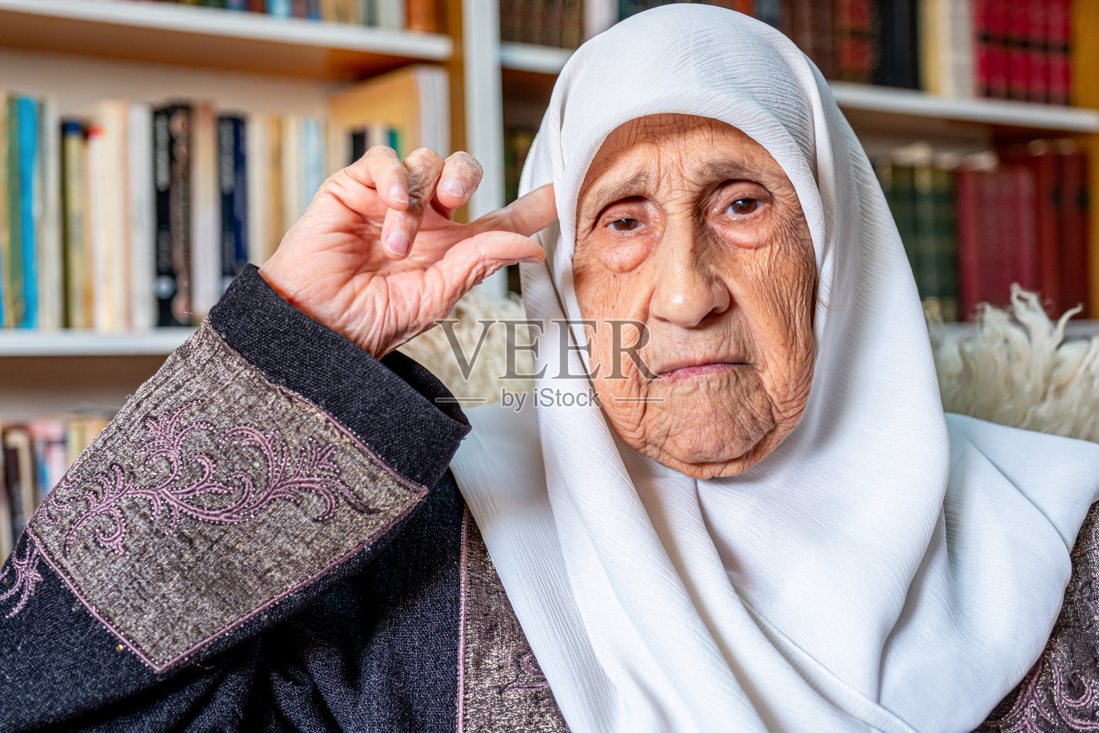 穿着传统服饰的老年女性坐在家中的图书馆里照片摄影图片