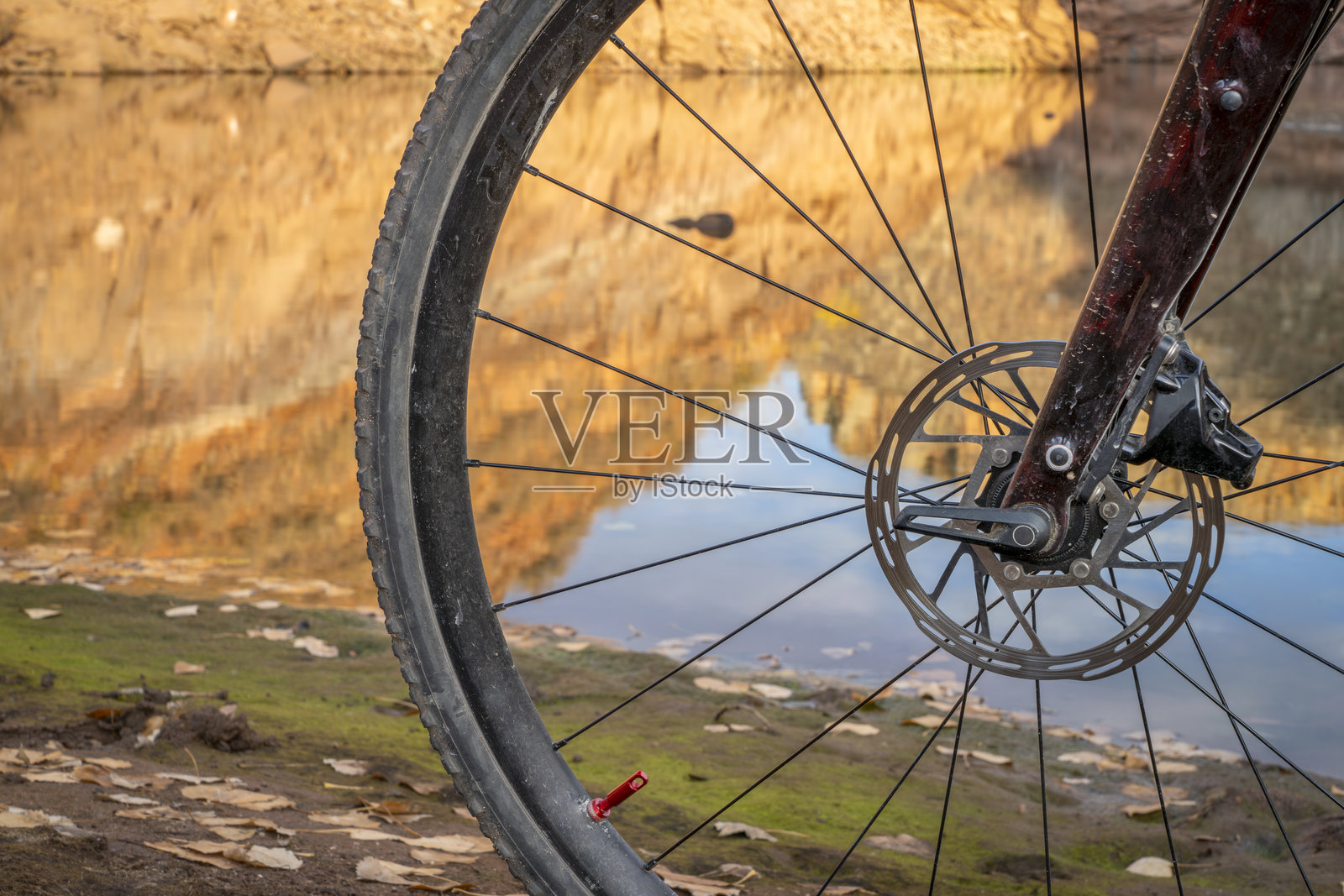 一辆泥泞的碎石自行车前轮停在湖边,湖面映出砂岩悬崖的倒影。照片摄影图片
