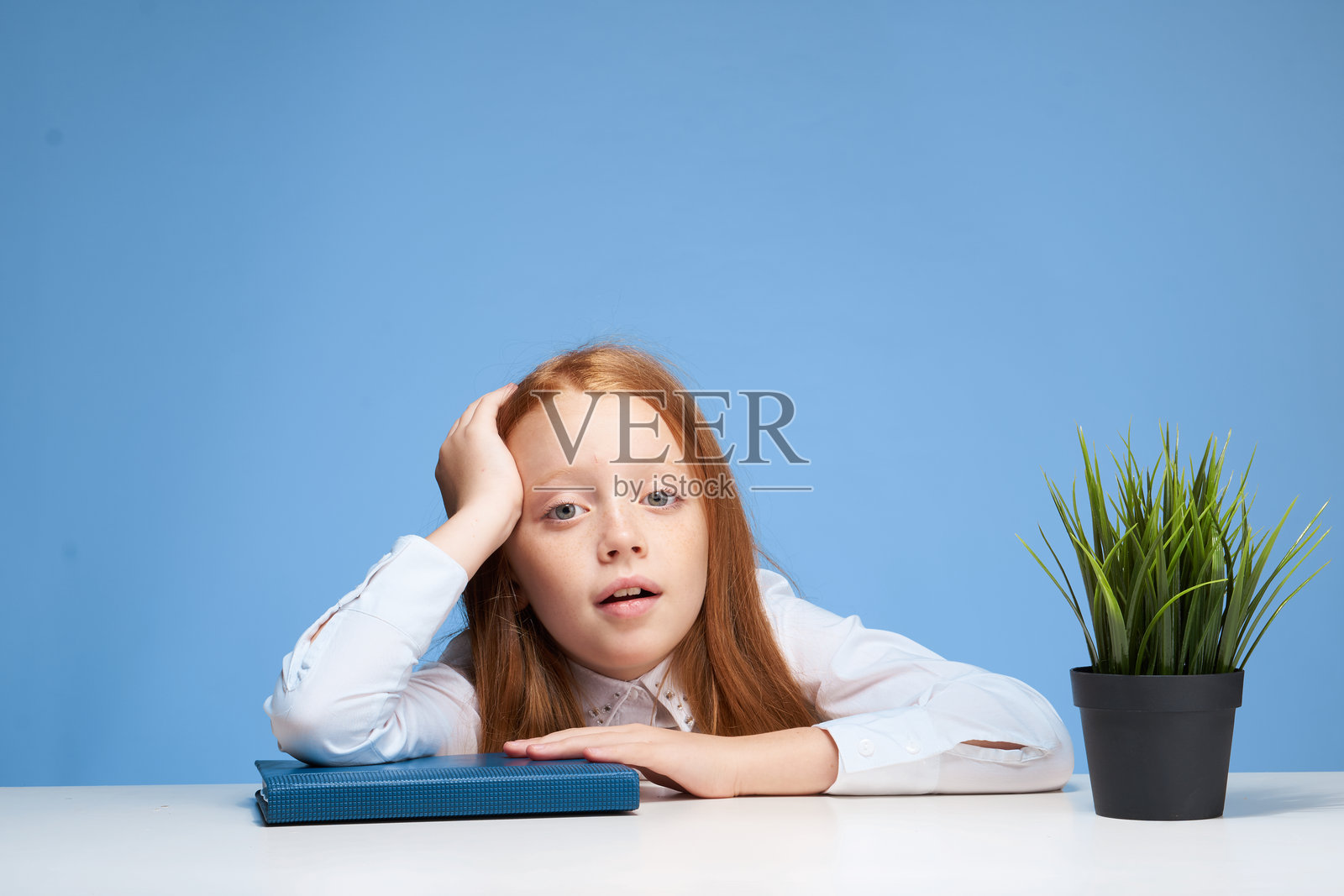 红发女孩坐在学校桌子旁,手中拿着书,正在学习。照片摄影图片