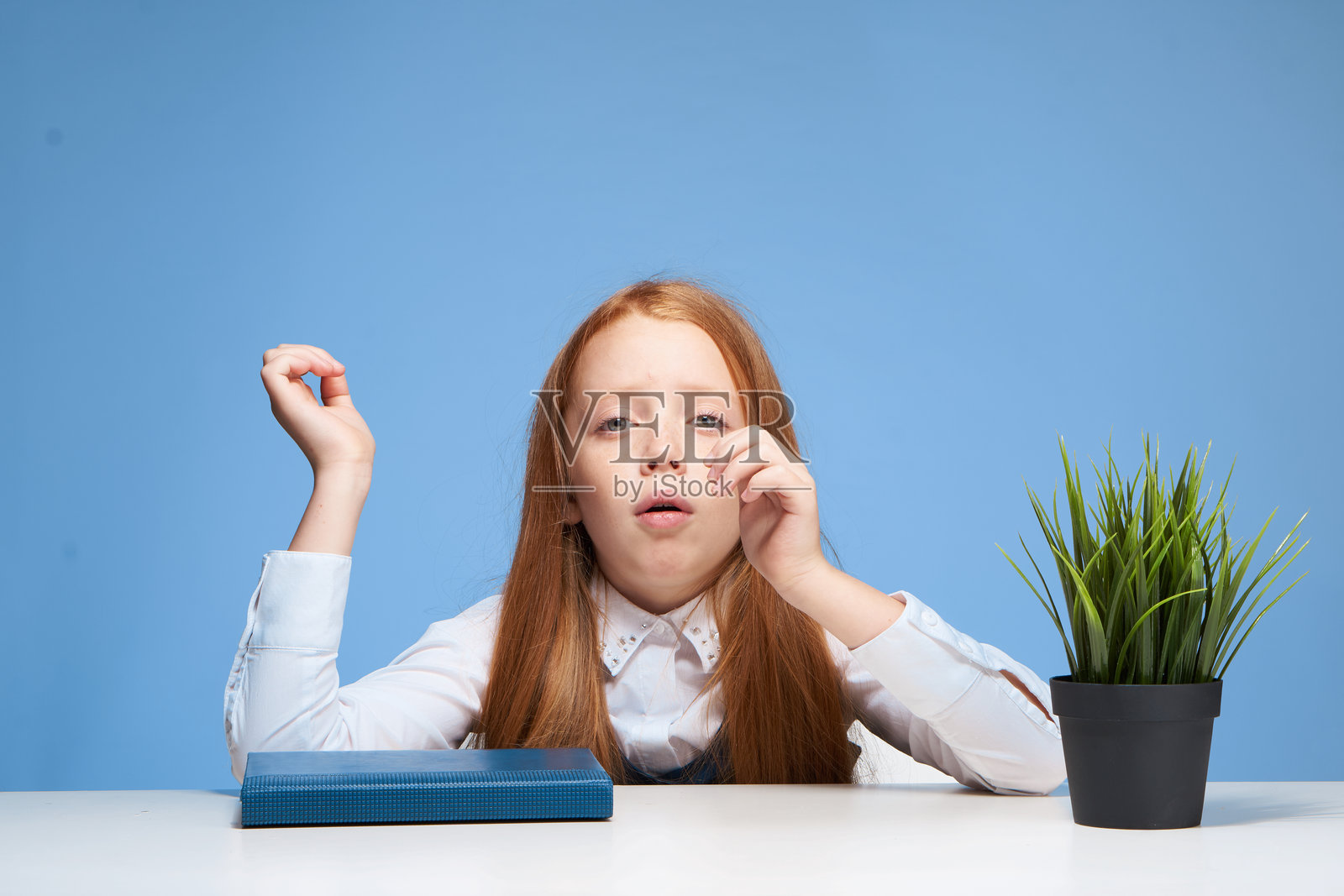 红发女孩坐在学校桌子旁,手中拿着书,正在学习。照片摄影图片