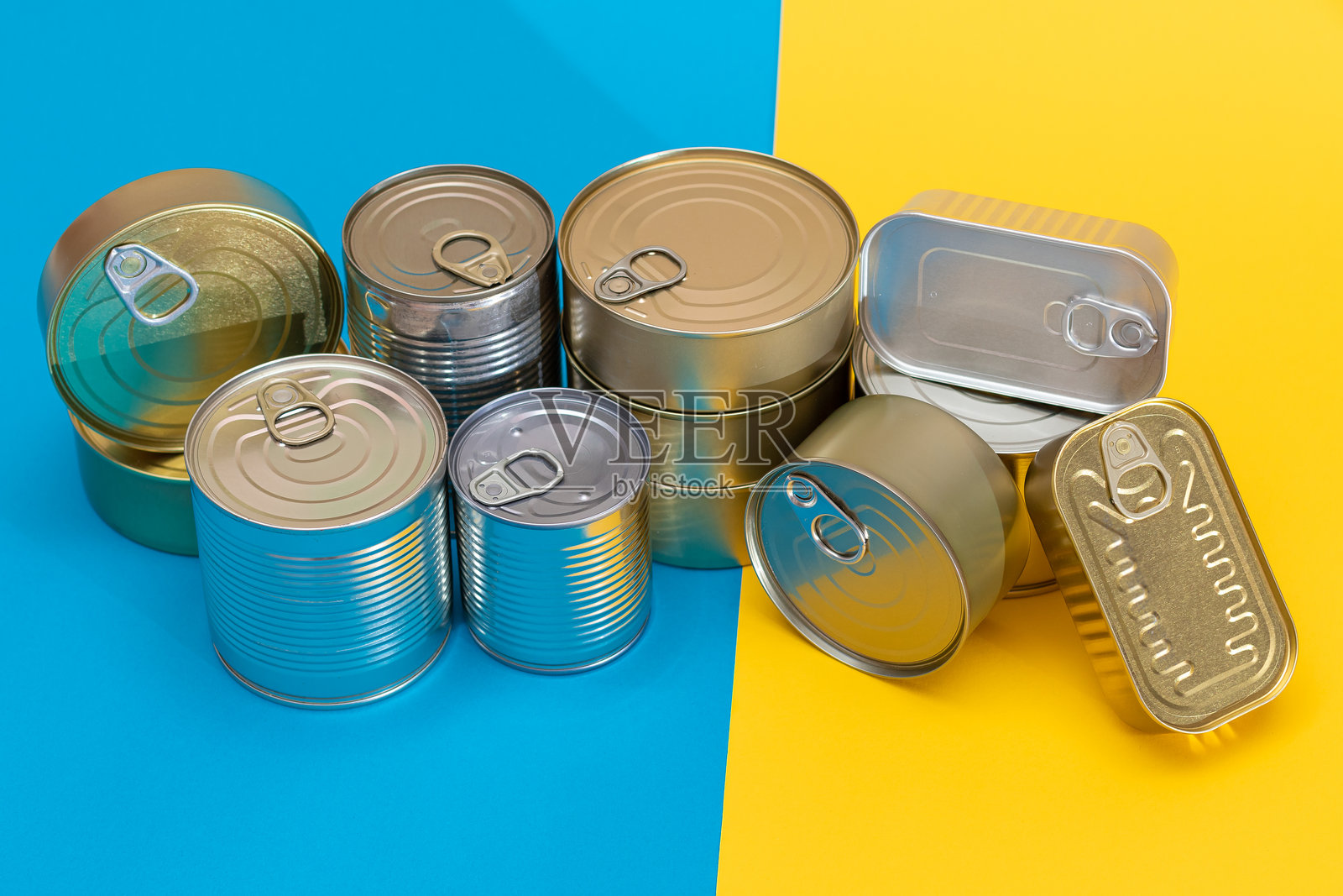 一组叠放的铁罐置于蓝色和黄色的分割背景上照片摄影图片