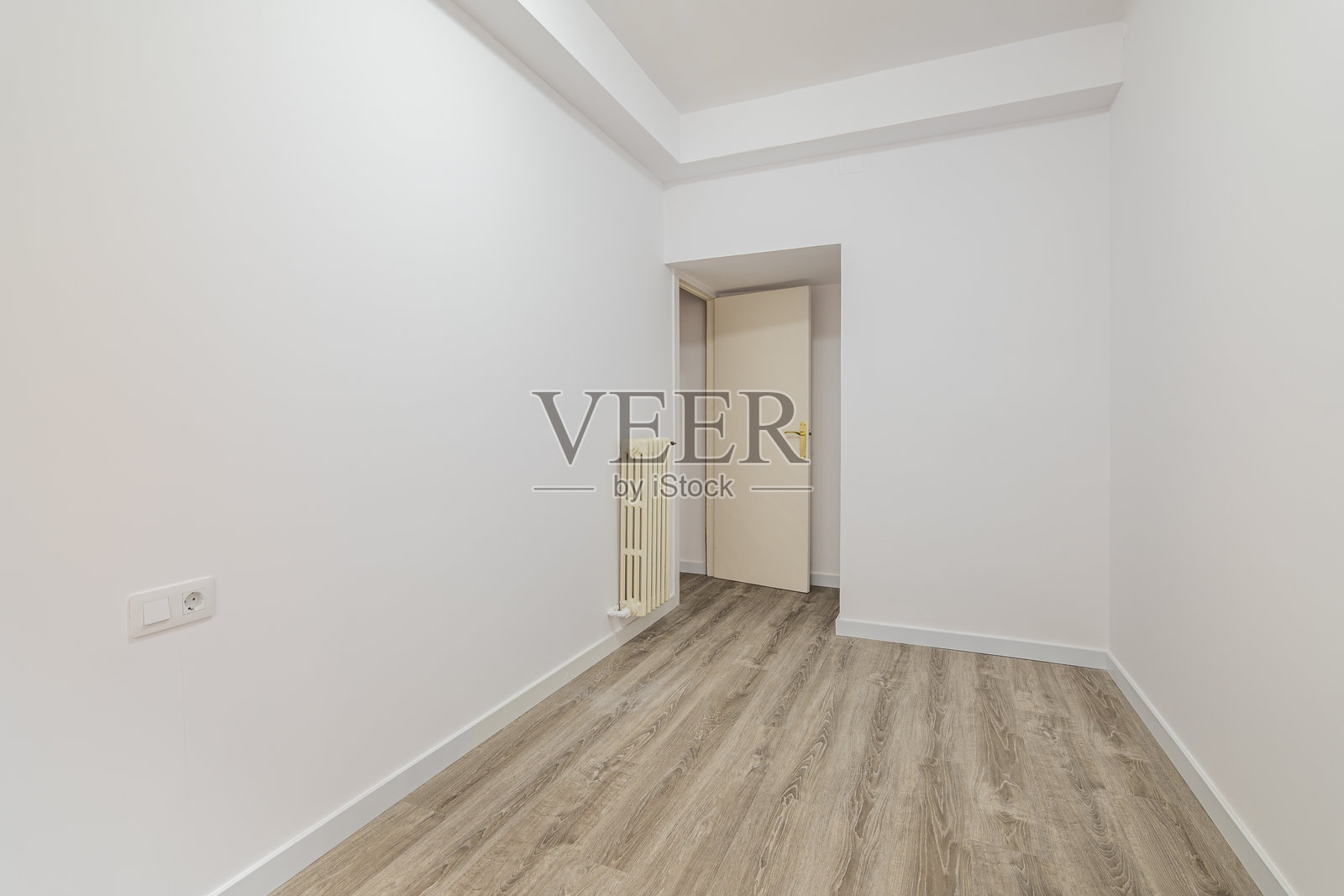 翻新公寓内空荡荡的房间,配有层压地板和新刷的白色墙壁,走廊通向其他房间。修理和施工概念。照片摄影图片