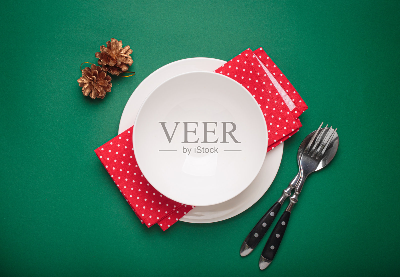 圣诞节桌面布置,空盘子、金色松果和红色餐巾在绿色背景上。照片摄影图片