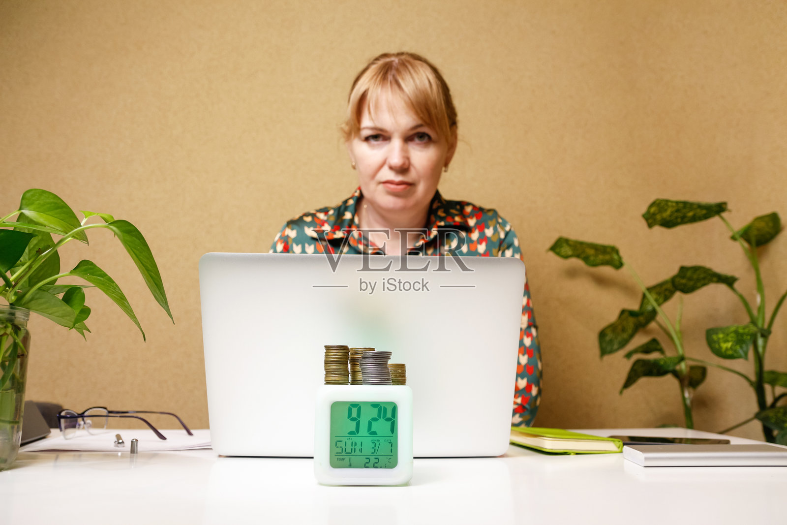 一位女性在办公室环境中使用笔记本电脑,旁边放着一堆硬币,表明财务管理和账户监控,适合与金融相关的博客。照片摄影图片